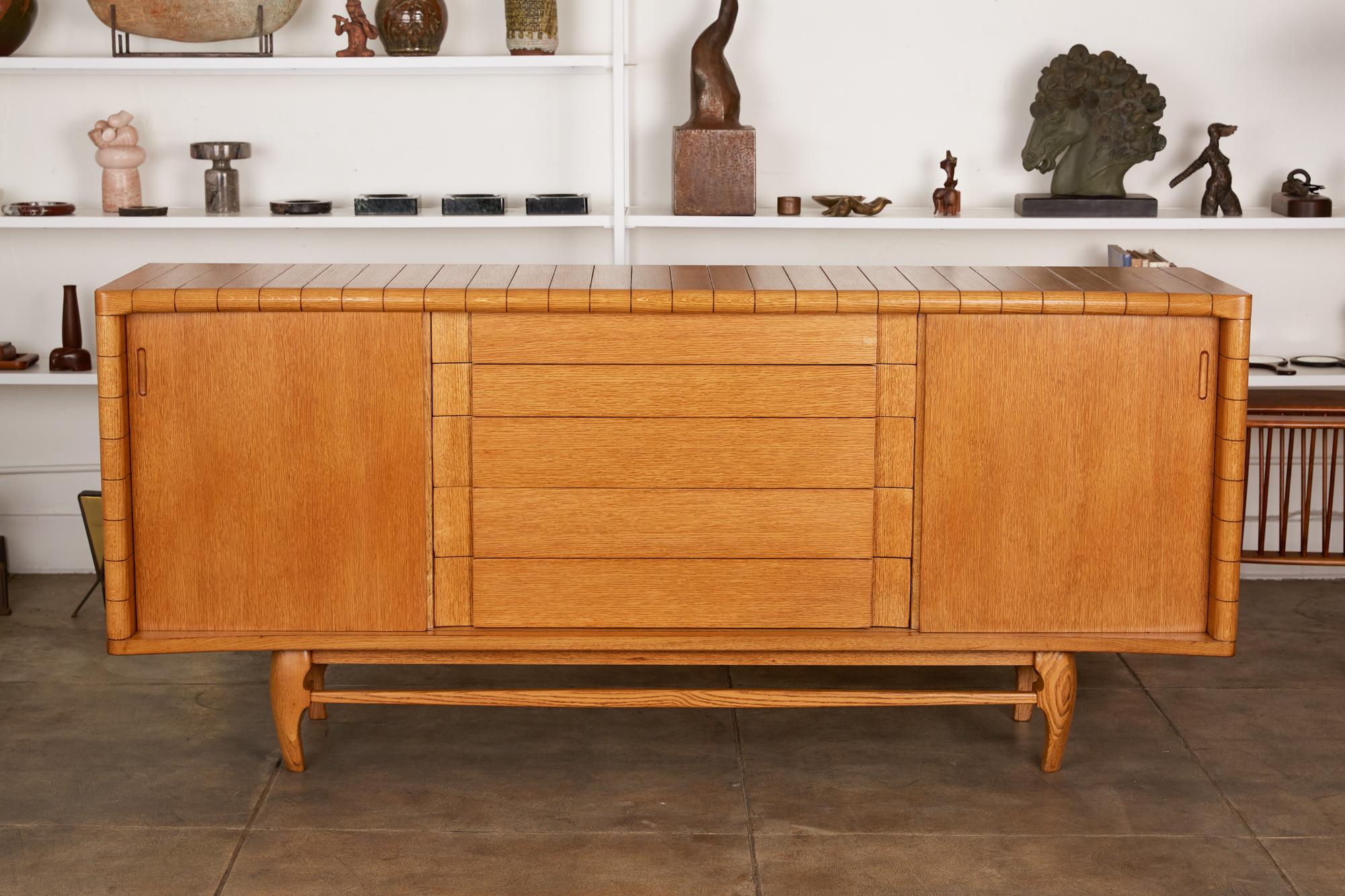 Harold Schwartz for Romweber credenza, USA, circa 1950s. The credenza has a solid oak frame with top and sides of the cabinet featuring channelled details and a concave front. The sliding doors reveal interior shelves while concealing the drawers,