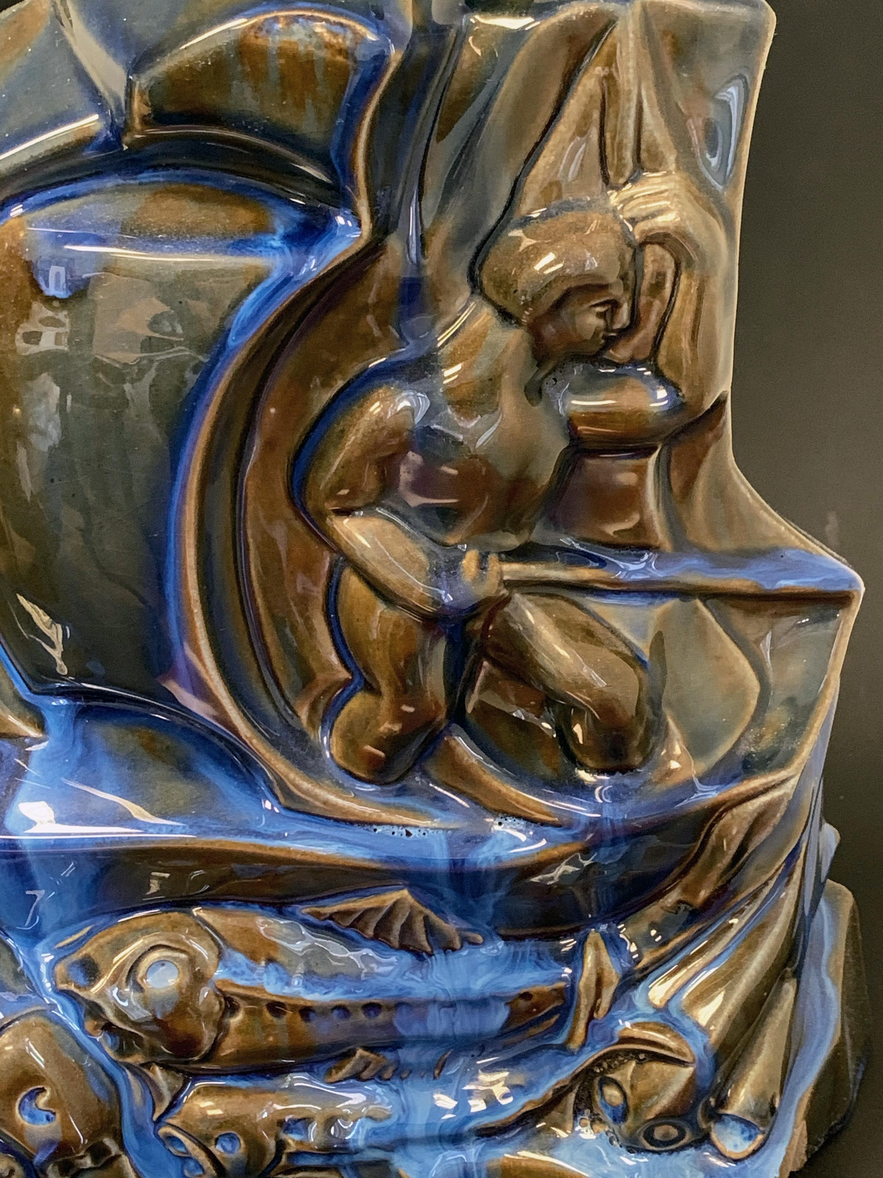 Rare and possibly unique, this extraordinary Art Deco sculpture is in the form of a sailing ship with a harpoonist on deck, the water below swarming with wide-eyed fish, all in navy blue, electric blue and olive drab glazes. The maker was Fulper