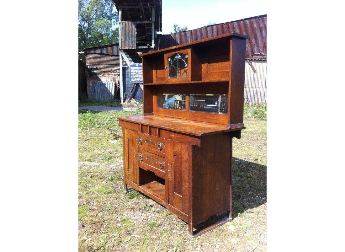 A good Arts and Crafts oak sideboard attributed to Harris Lebus with stylised Glasgow Style stain glass to the upper cupboard and 2 open shelves, with two central drawers with copper strap handles and further storage below flanked by a pair of