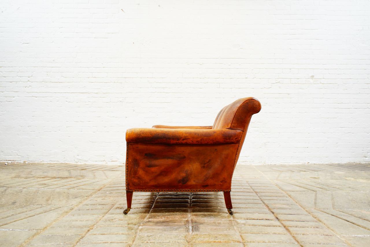 Harrods of London chestnut brown leather three seat sofa, circa 1910, characterful leather patina, the turned legs terminating in brass castors stamped 'Harrods, London'.

The back leg has a historic invisible repair, and the front edge leather