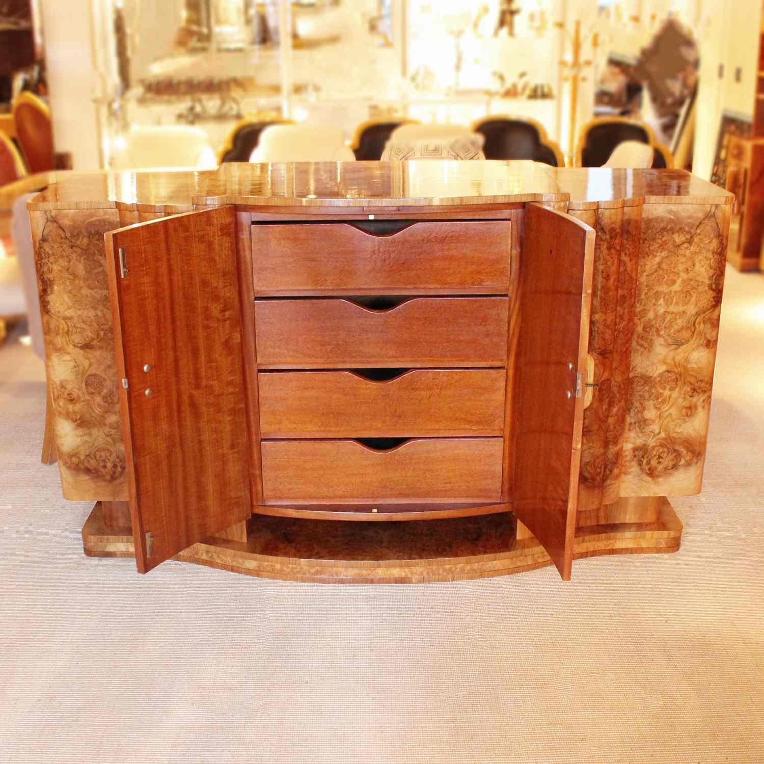 An Art Deco sideboard in burr walnut with original wooden handles. Central cabinet opens to a set of mahogany lined drawers. The right cabinet opens to a bottle turntable and the left side to mahogany lined shelves. Bow fronted with reeded detail.