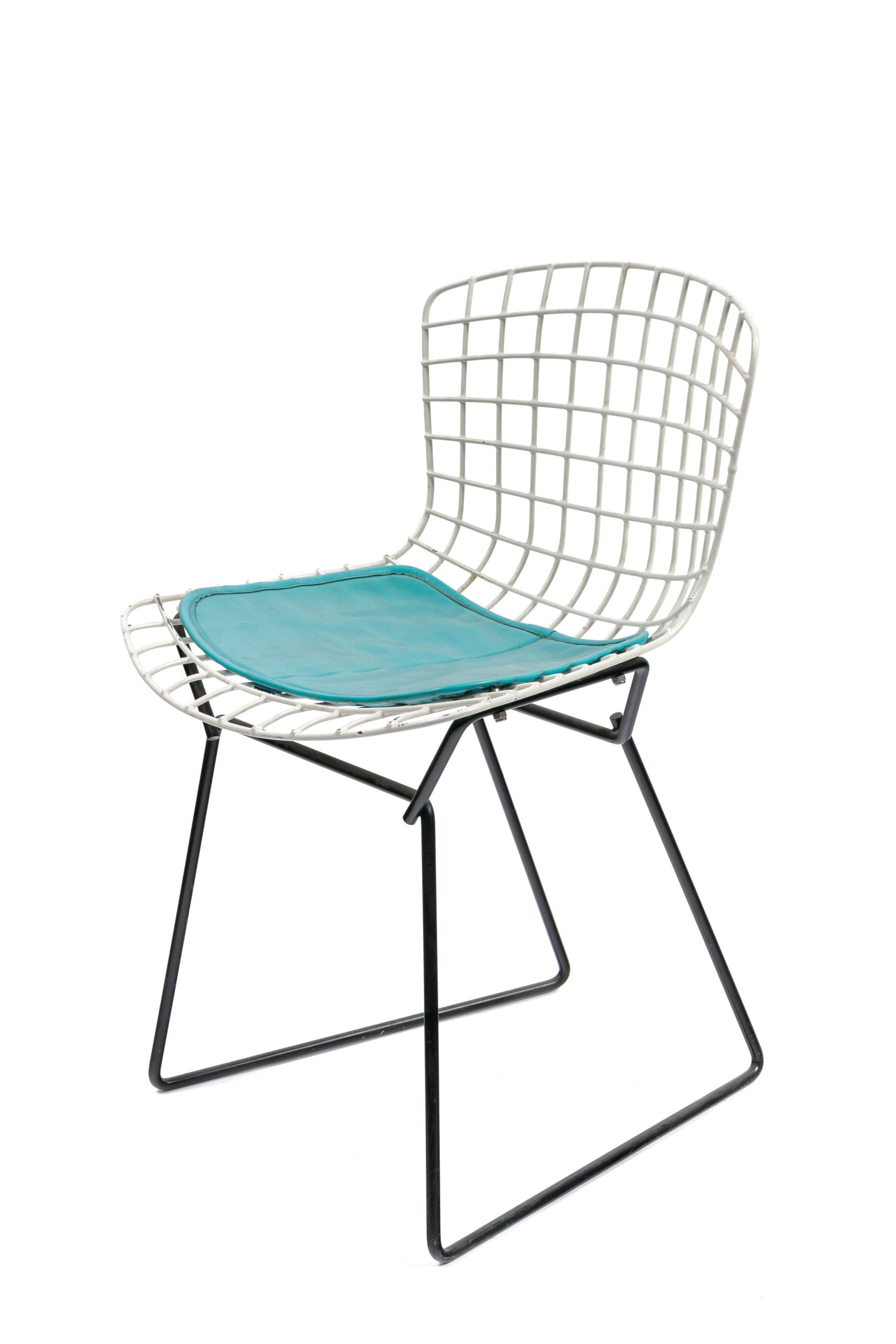 A universally recognized design, this Bertoia child's chair has a white seat with a black base and the original turquoise seat pad.