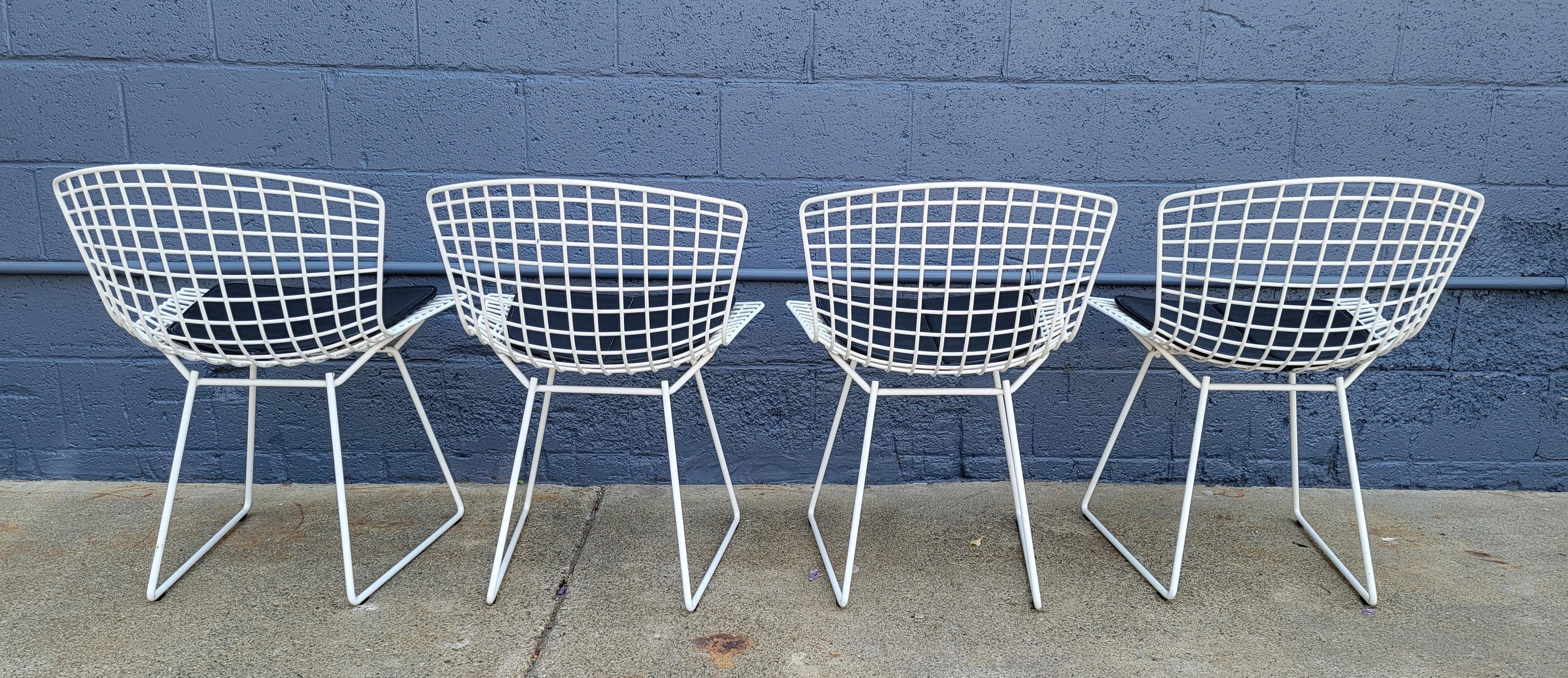 A vintage set of 4 wire dining chairs designed by Harry Bertoia for Knoll. White frames with original black seat cushion. Good vintage condition with age appropriate wear from use.