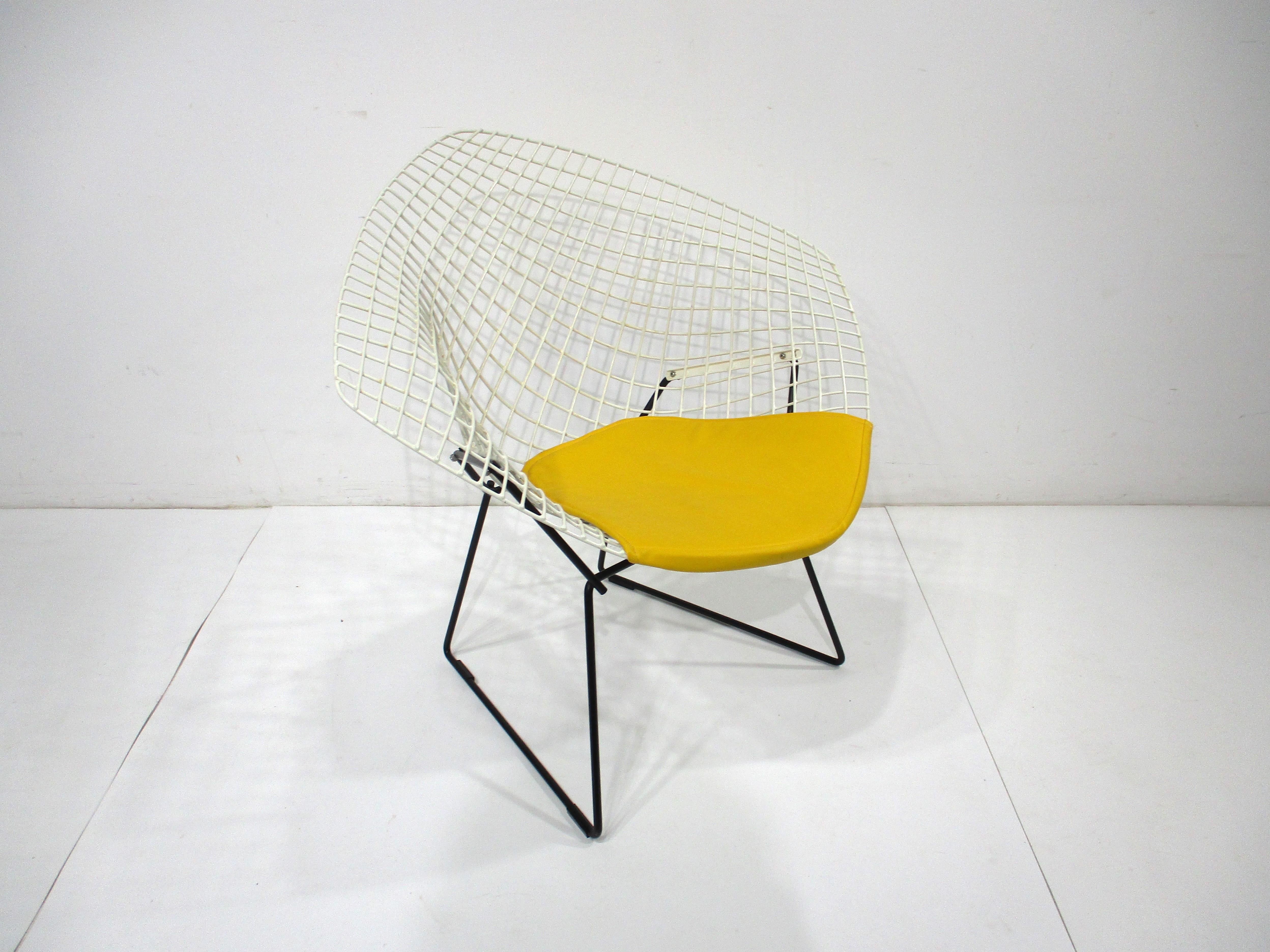 A white plastic coated welded wire diamond lounge chair with a contrasting satin black base and sunflower yellow leatherette seat pad . Manufactured by Knoll International and designed by iconic artist , furniture designer and architect Harry