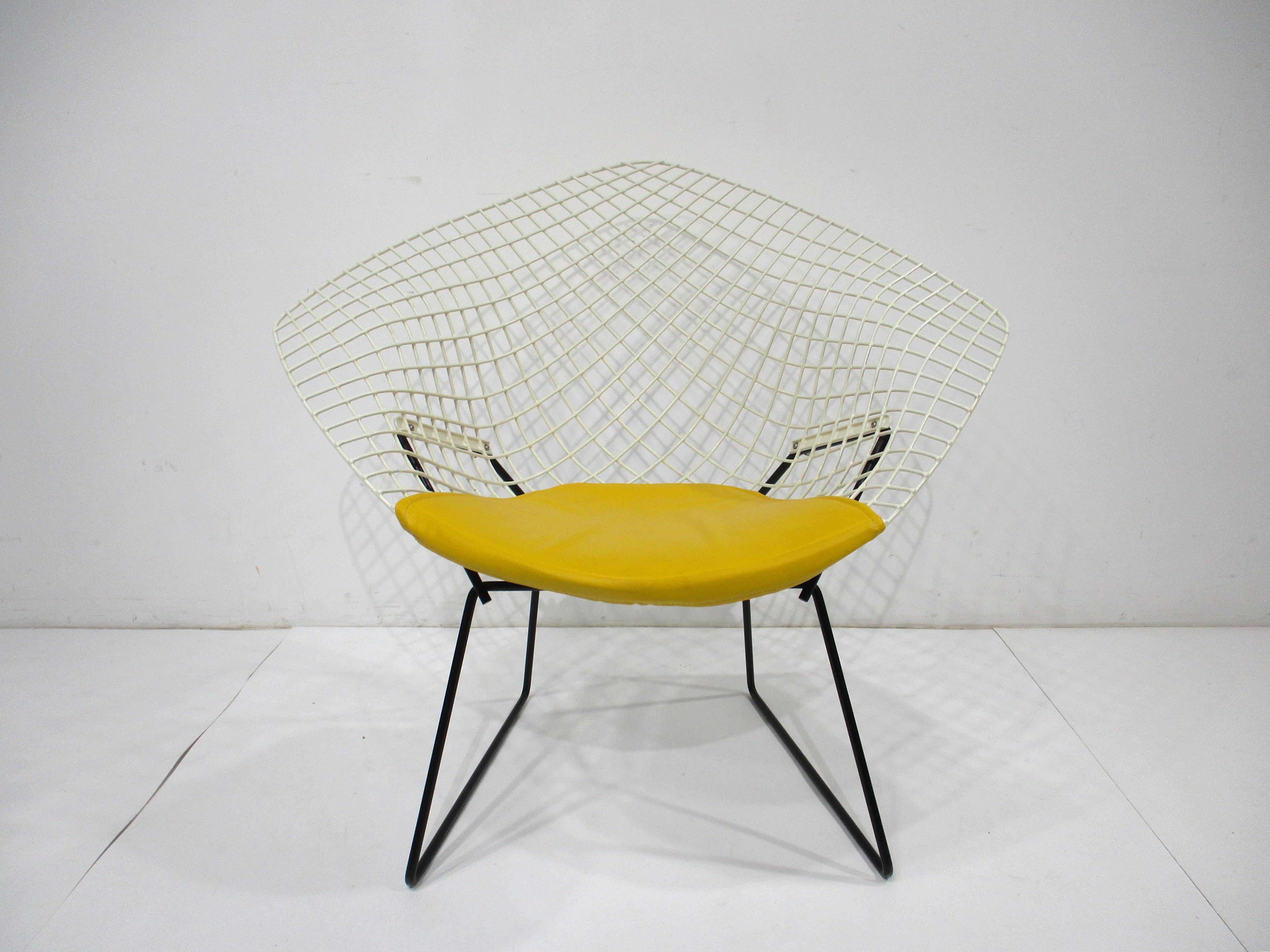 A white plastic coated welded wire diamond lounge chair with a contrasting satin black base and sunflower yellow leatherette seat pad . Manufactured by Knoll International and designed by iconic artist , furniture designer and architect Harry