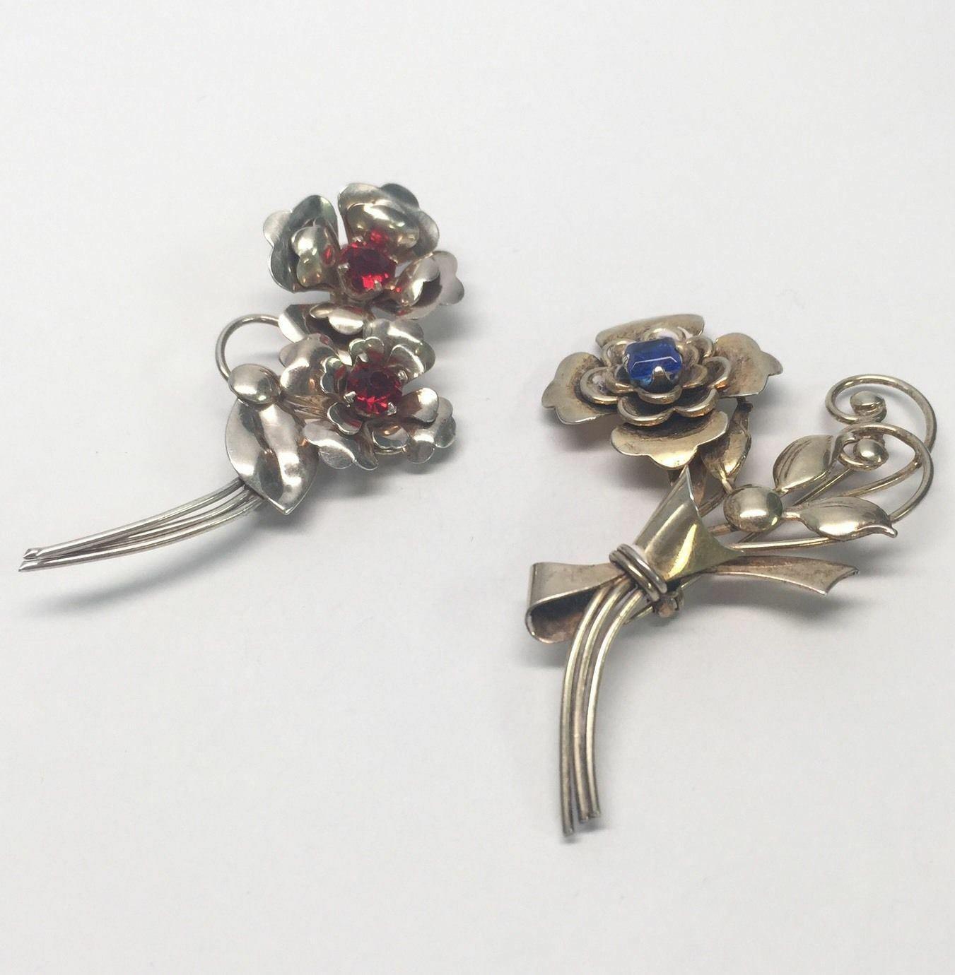Harry Iskin 1940's sterling silver pair of flower pins/brooches. These brooches include red and blue rhinestones set in the center of the flowers.

Marking: HI, STERLING.

Red pin measures approx. 2 1/2