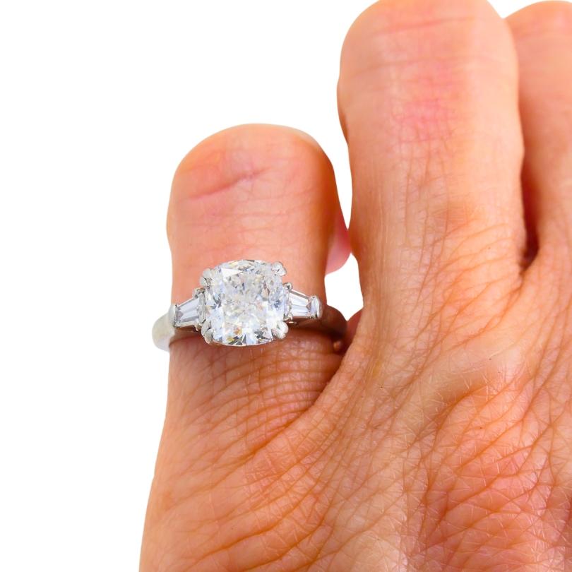 Bague de fiançailles Harry Winston, en platine, mettant en valeur un diamant taille coussin de 1,77 carat. Deux diamants baguettes effilés encadrent la pierre centrale. Ces diamants angulaires complètent la forme du diamant de taille coussin tout en