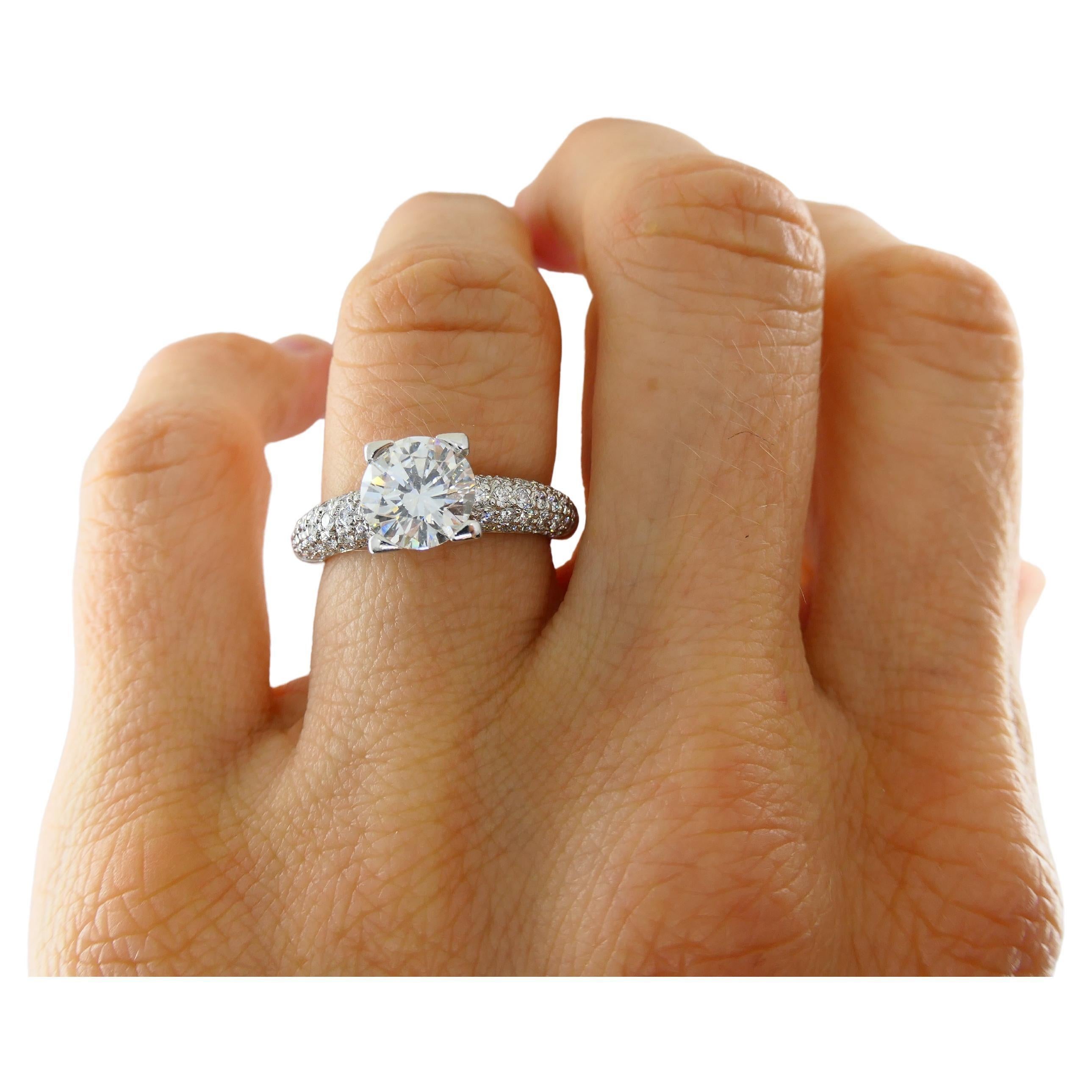 A beautiful Harry Winston engagement ring, crafted in platinum, featuring a central diamond weighing 1.50 carats. The brilliance of the centerpiece is enhanced by pavé diamonds set along the band, totaling an additional 0.53 points. The central