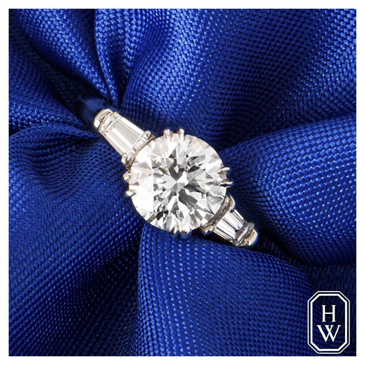 A captivating platinum diamond engagement ring by Harry Winston from the Classic collection. The three stone ring features a round brilliant cut diamond set to the centre in a 4 claw mount weighing 1.51ct, E colour and VS2 clarity. The centre