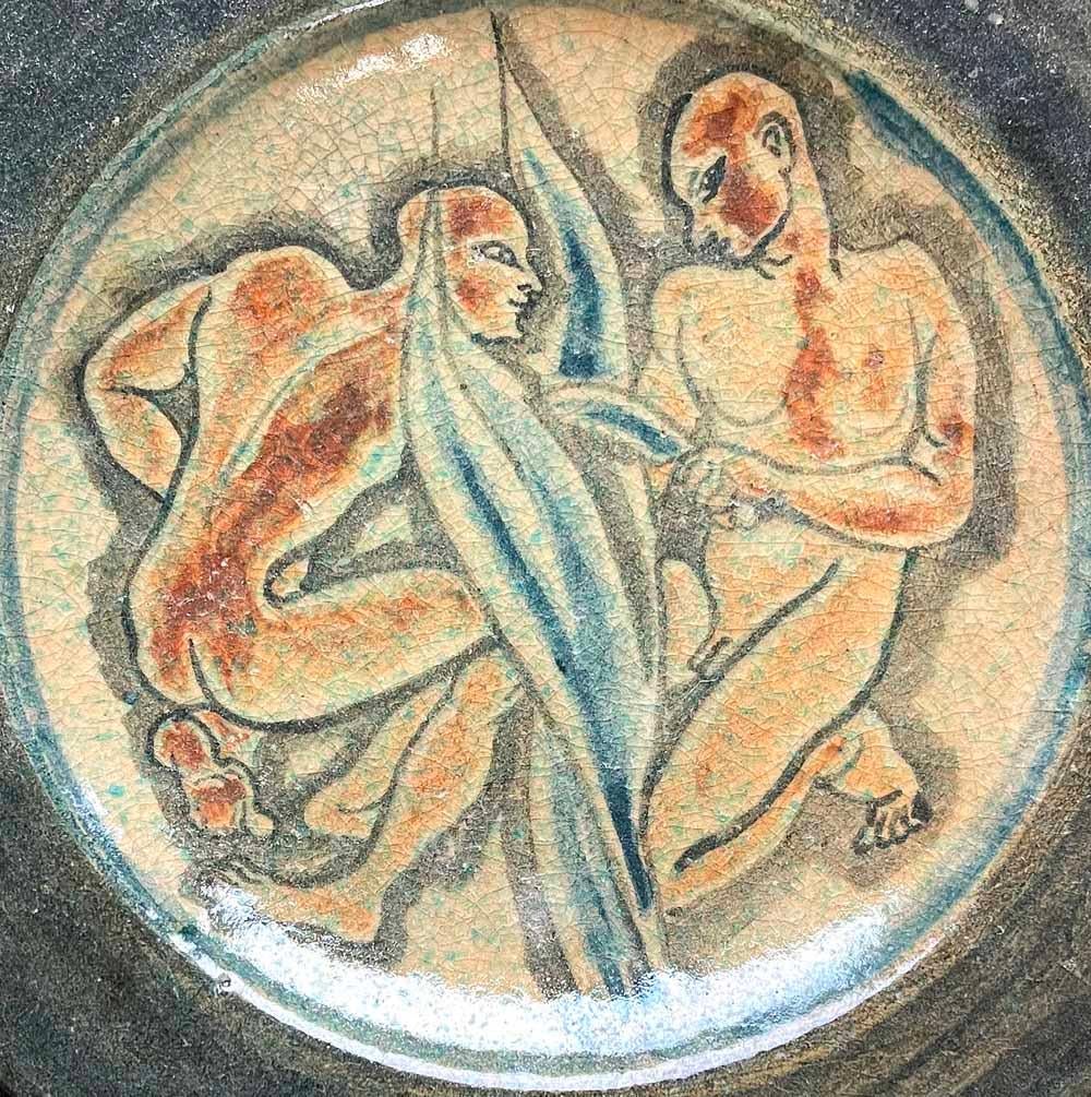 Unique and striking, this wall plate by the famed Lachenal ceramic works in France depicts two nude male figures harvesting lush, broad-leafed plants in the field. The artist was clearly a painter and signed the piece 