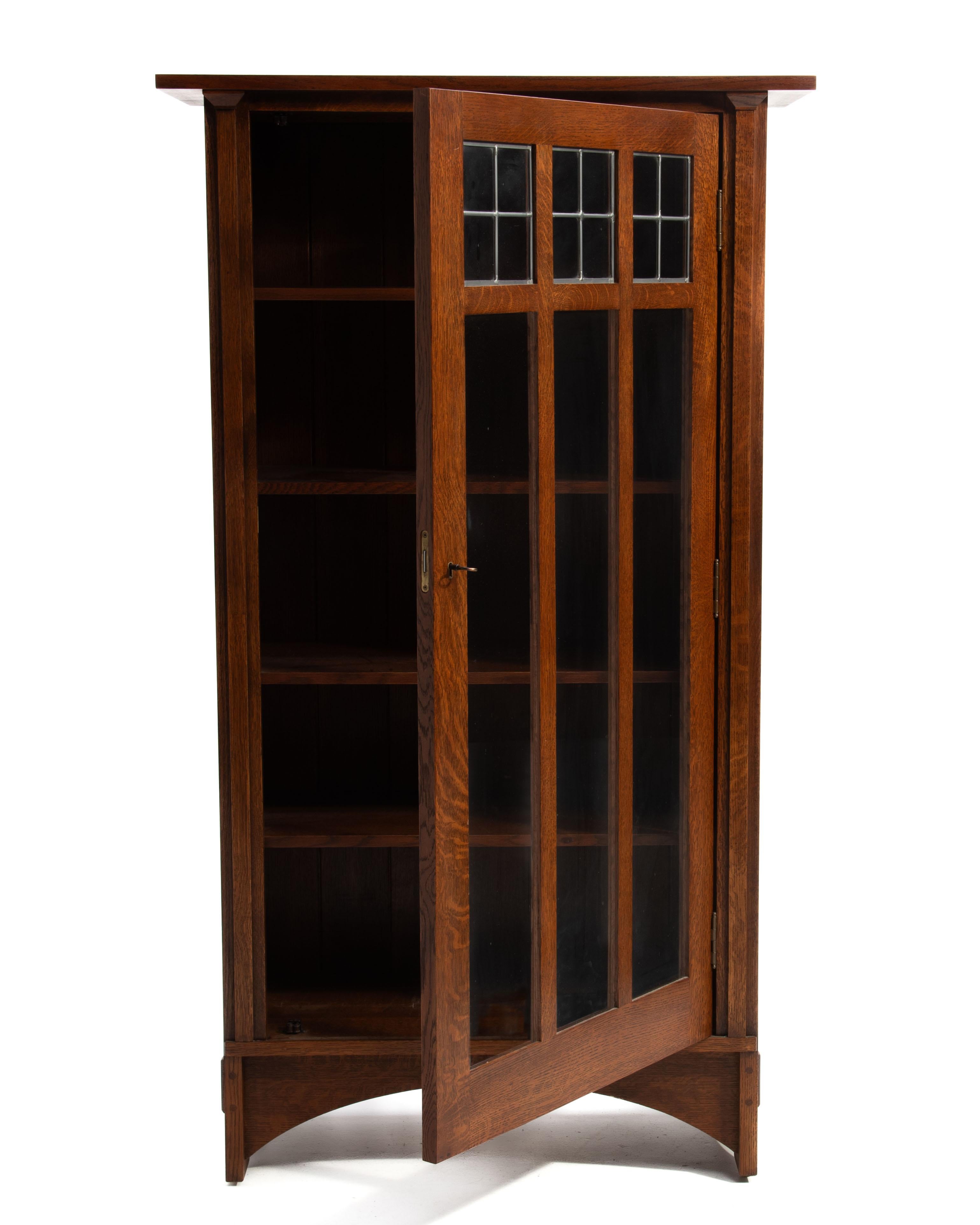 The iconic Gustav Stickley single door bookcase designed by Harvey Ellis. Overhanging top, mortise and tenon construction, arched stretcher, quarter sawn oak, lead glass windows, adjustable shelves, chamfered ship lap planking back and the original