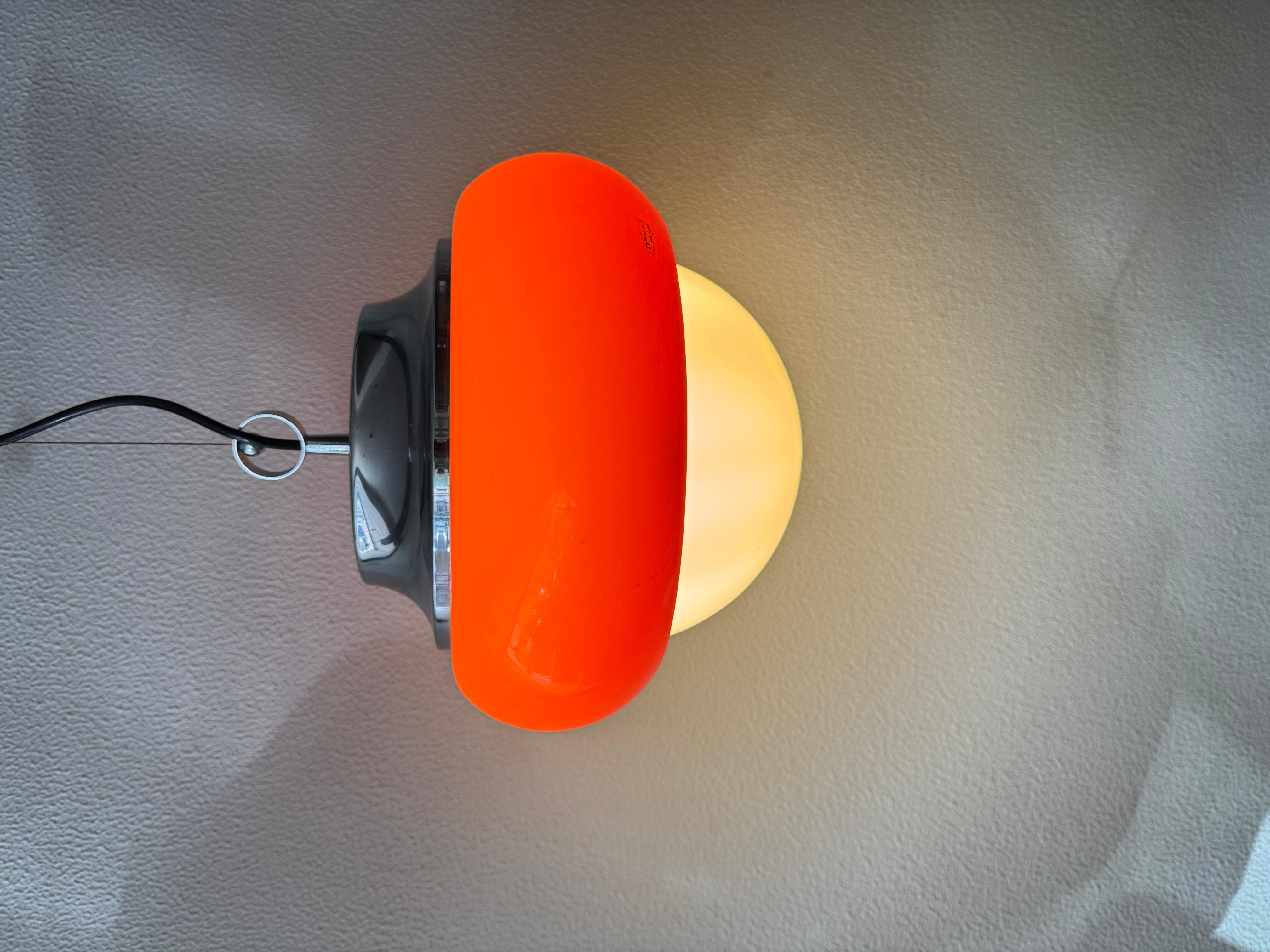 Questa autentica lampada a sospensione Art. 3030 di Harvey Guzzini è stata prodotta in Italia nei primi anni Settanta. Classico esempio dell'estetica A Space Age del marchio, la lampada combina un paralume in acrilico arancione vivo con un diffusore