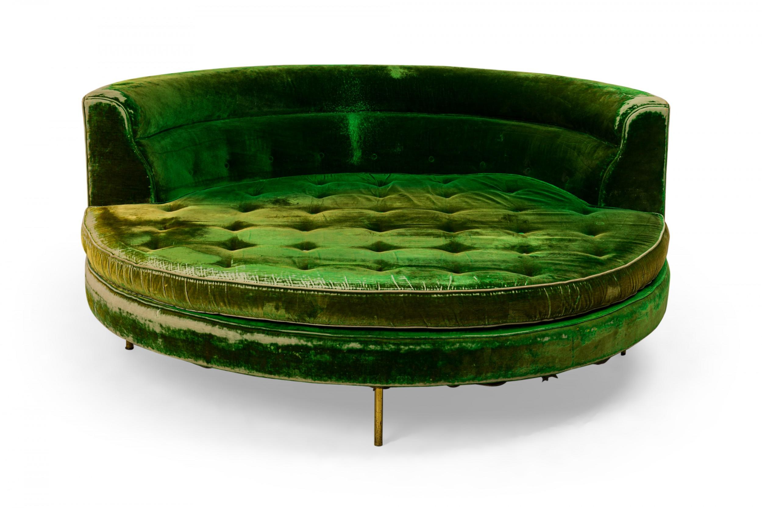 American Mid-Century large round sofa with a low curved partial backrest and emerald green velvet upholstery with a button tufted removable seat cushion, resting on five short brass dowel legs. (HARVEY PROBBER)
