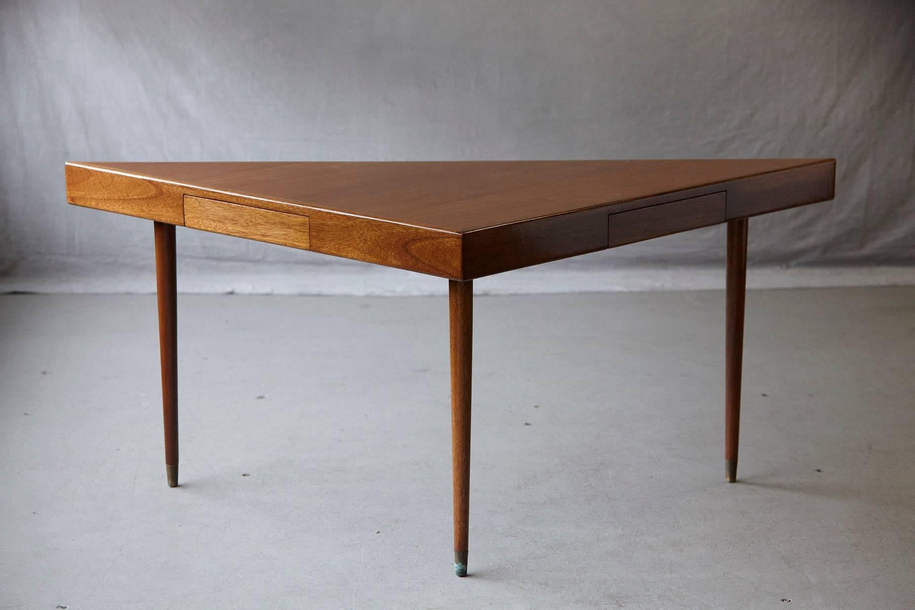Beautiful, newly refinished, bleached mahogany triangular table by Harvey Probber. 
Immaculate top with two drawers based on slightly tapered legs with unpolished brass sabots (can be polished if wished). Designer's label in the drawer.