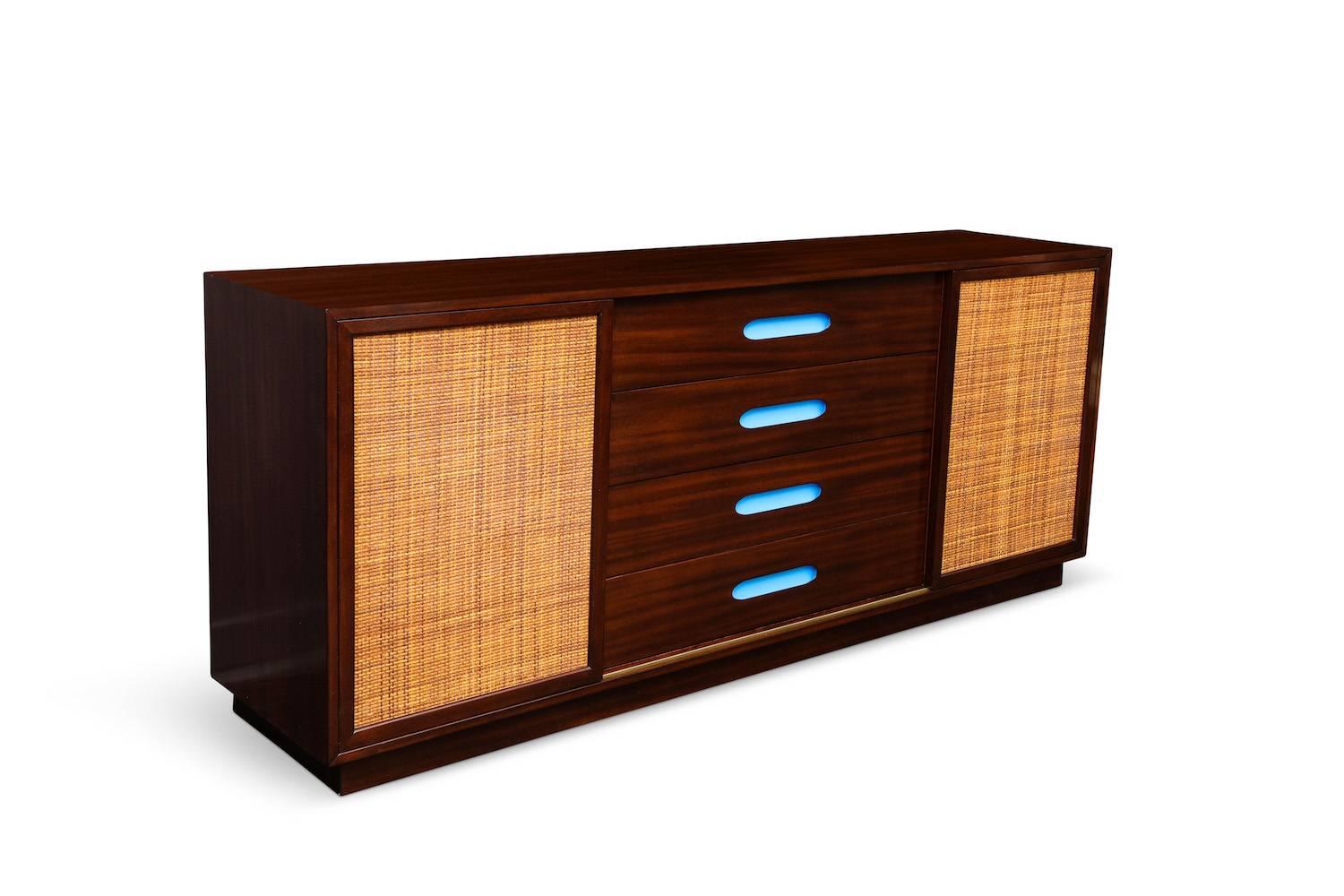 Unusual storage cabinet by Harvey Probber.
Dark stained mahogany cabinet with sliding rattan doors and four centre drawers. Each rattan door slides to reveal a unique bank of drawers, one set lined with cork. Centre drawers with inset pulls painted