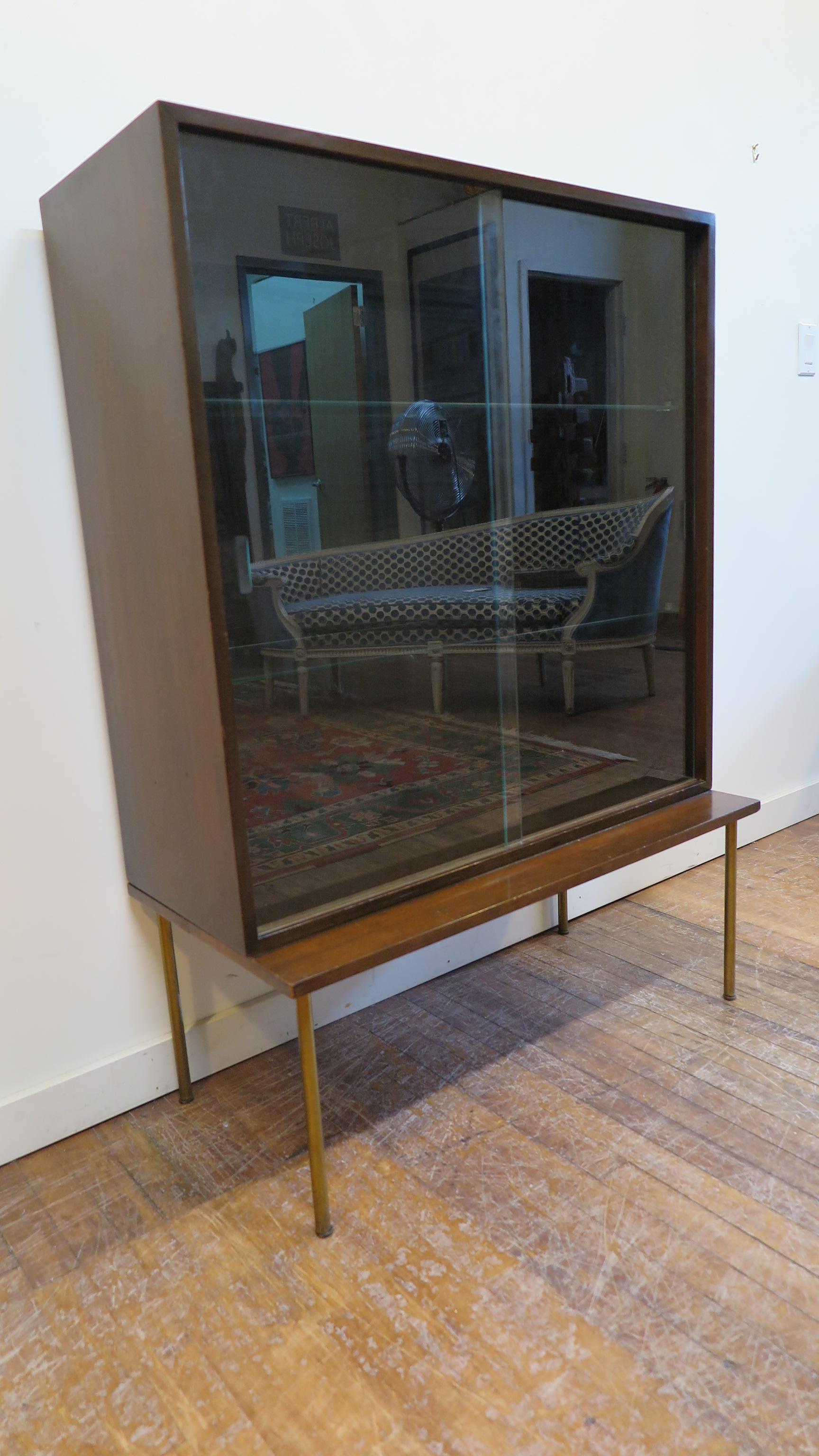 Harvey Probber cabinet with glass doors, two glass shelf's in a case set on stand with brass legs. This cabinet is in good original condition. Glass doors lift out easily if desired open face cabinet or display. Some fading, small dings, light