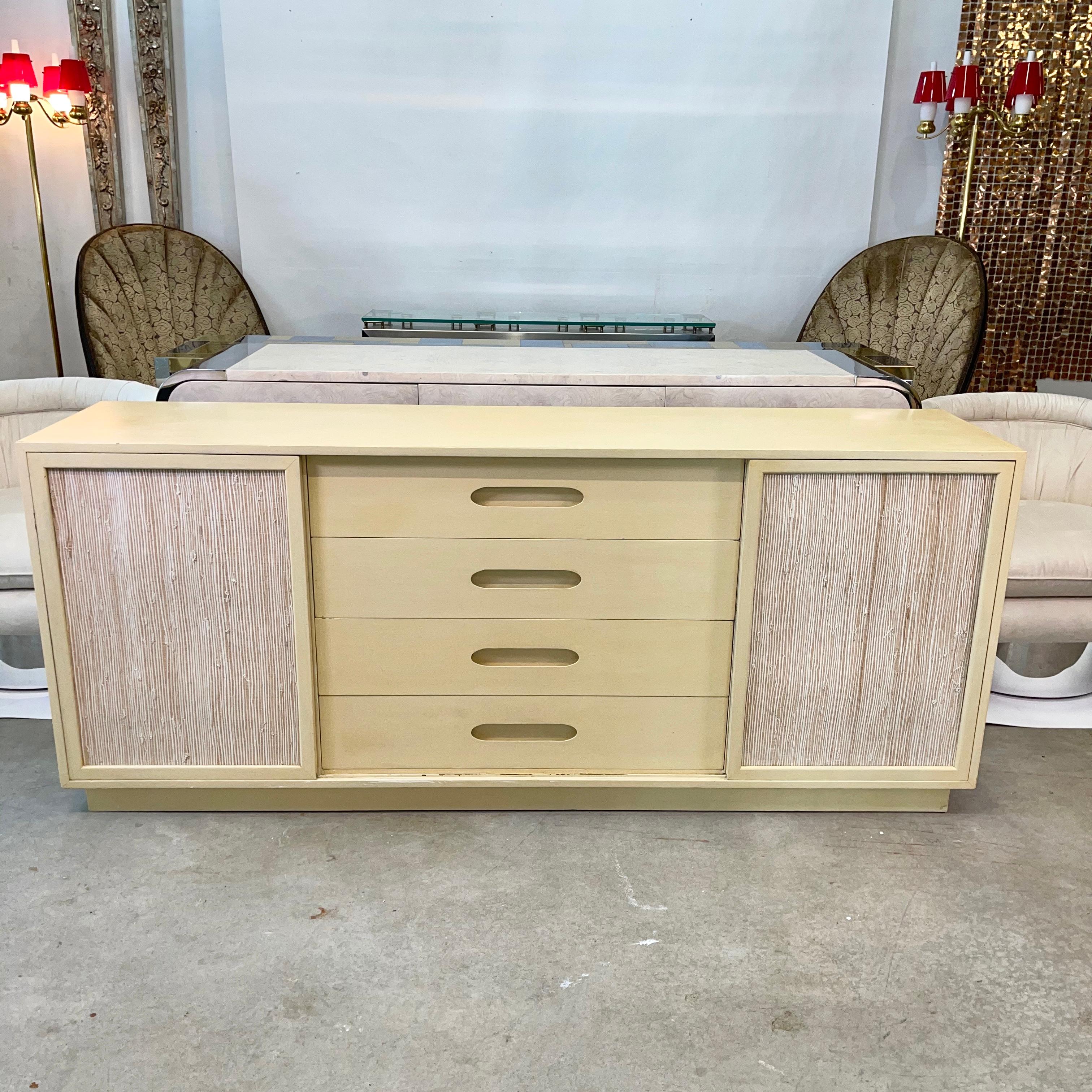 Mid-Century Modern dresser by Harvey Probber in grain painted blonde mahogany with four matching large center drawers having distinctive Probber recessed pulls and two sliding doors paneled in rough textured grasscloth, concealing four white