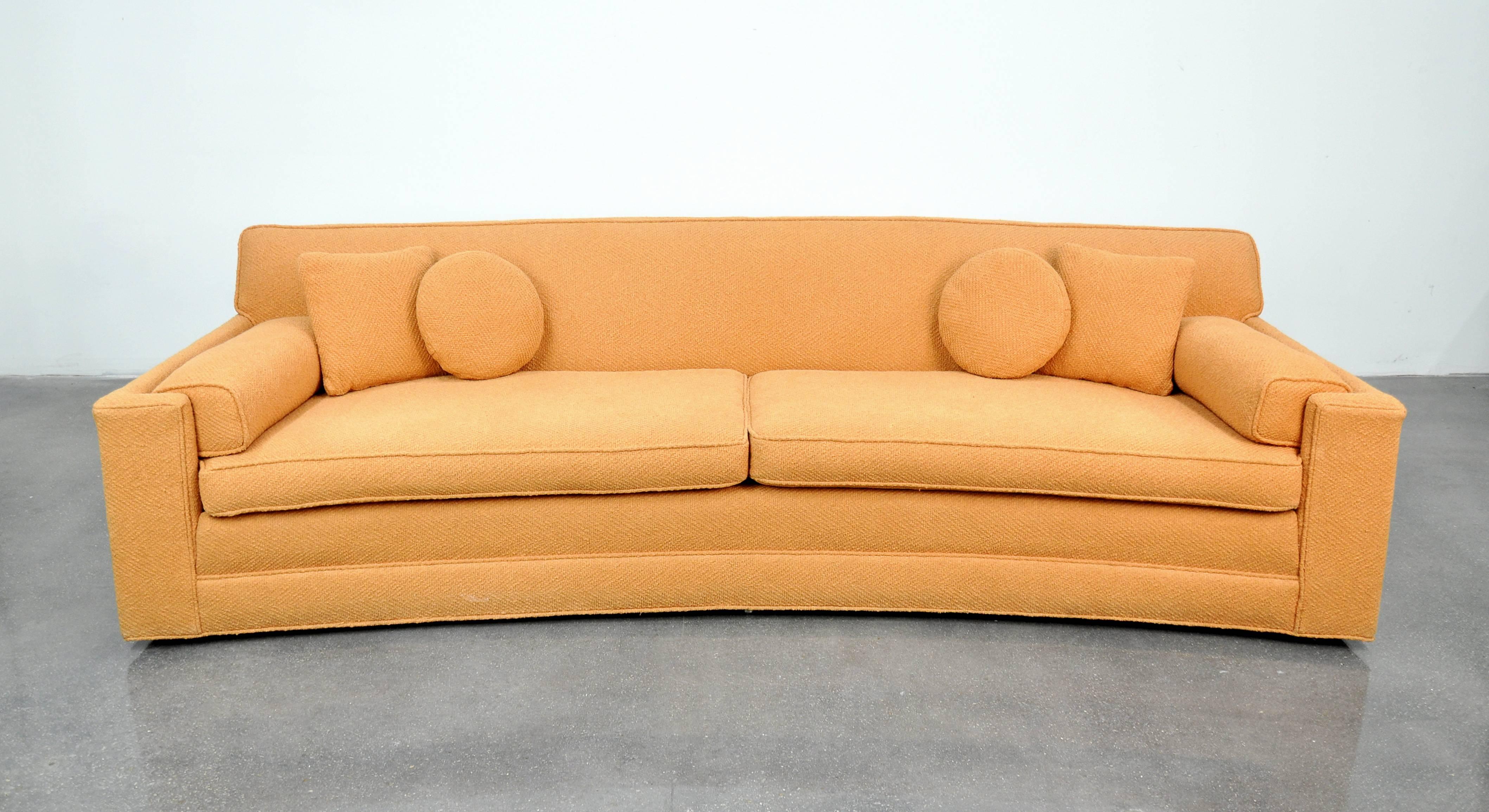 A unique vintage Mid-Century Modern pastel coral sofa attributed to Harvey Probber, and dating from the 1950s. The salmon couch features a crescent shape with angular armrests and low profile casters. The curvilinear light peach orange sofa has