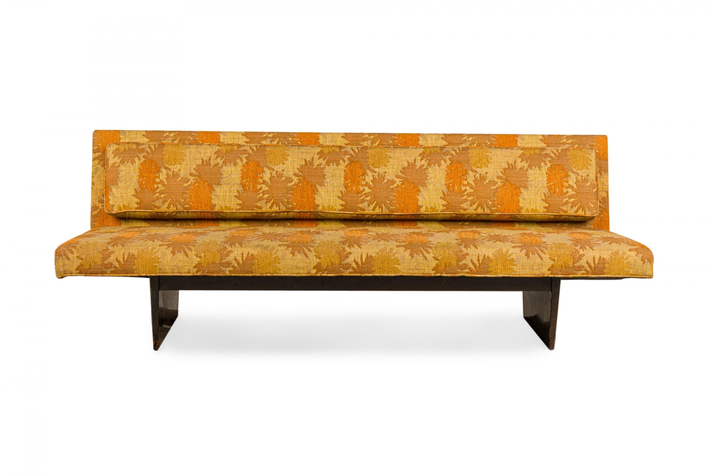 Canapé américain du milieu du siècle avec une tapisserie à motifs de soleils orange, jaune et or, reposant sur une base de traîneau en bois ébonisé. (HARVEY PROBBER).
 