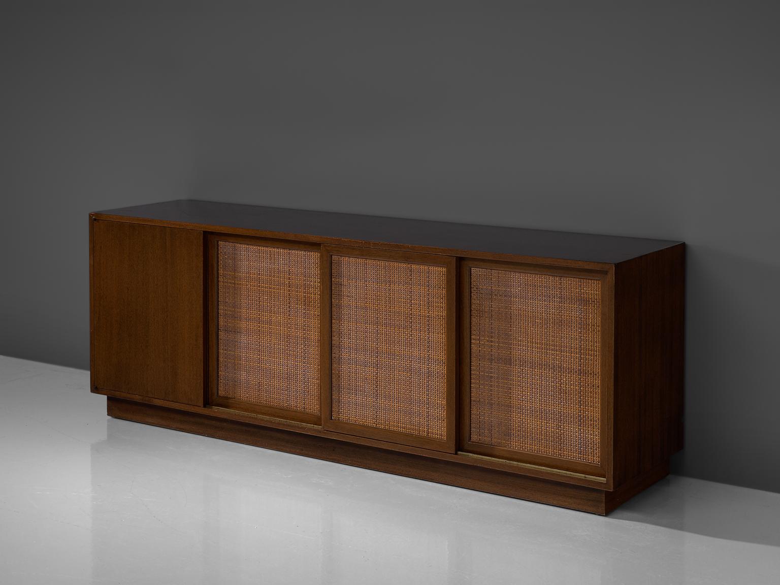 Harvey Probber, sideboard, mahogany and rattan, United States, 1950s.

A storage cabinet with rattan doors sliding open to reveal three compartments of shelves and drawers, and featuring a cabinet containing a metal trash bin. This cabinet has a