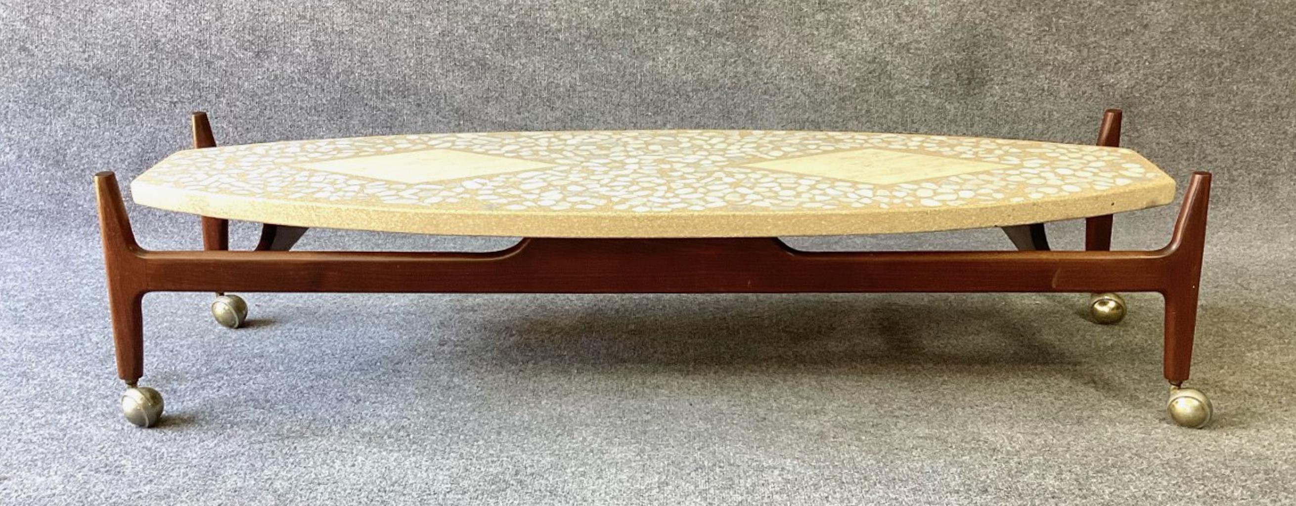 A striking Mid-Century Modern rolling cocktail table designed by Harvey Probber, dating from the 1960s. It features a boat-shaped terrazzo top inlaid with Italian travertine diamonds and marble chips over a sculptural walnut base with casters. The