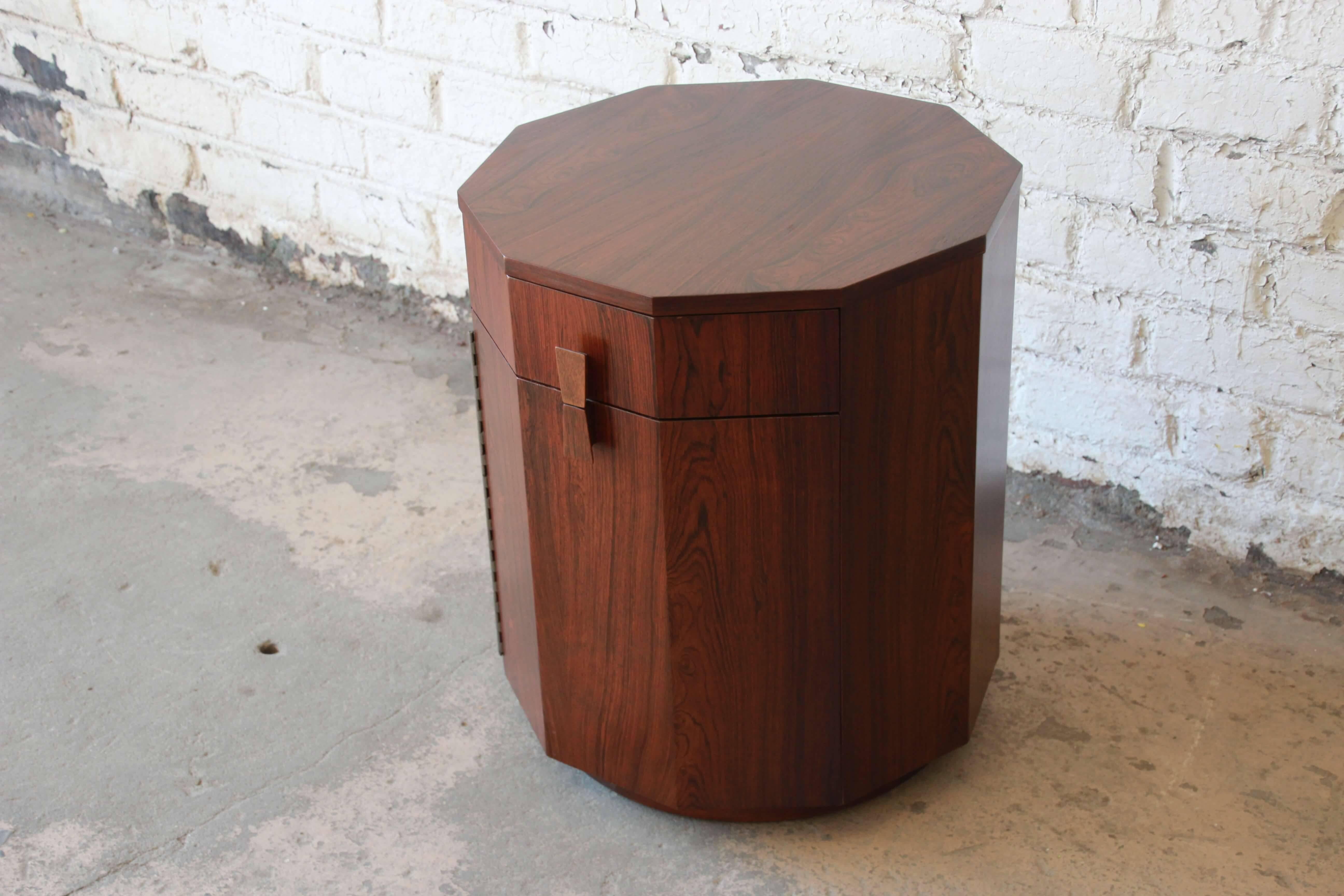 Offering a stunning decagon dry bar in rosewood by Harvey Probber. This piece can serve as an end table or other creative use and has plenty of space for your fine liquor storage. The lower cabinet door opens to an ebonized interior with available
