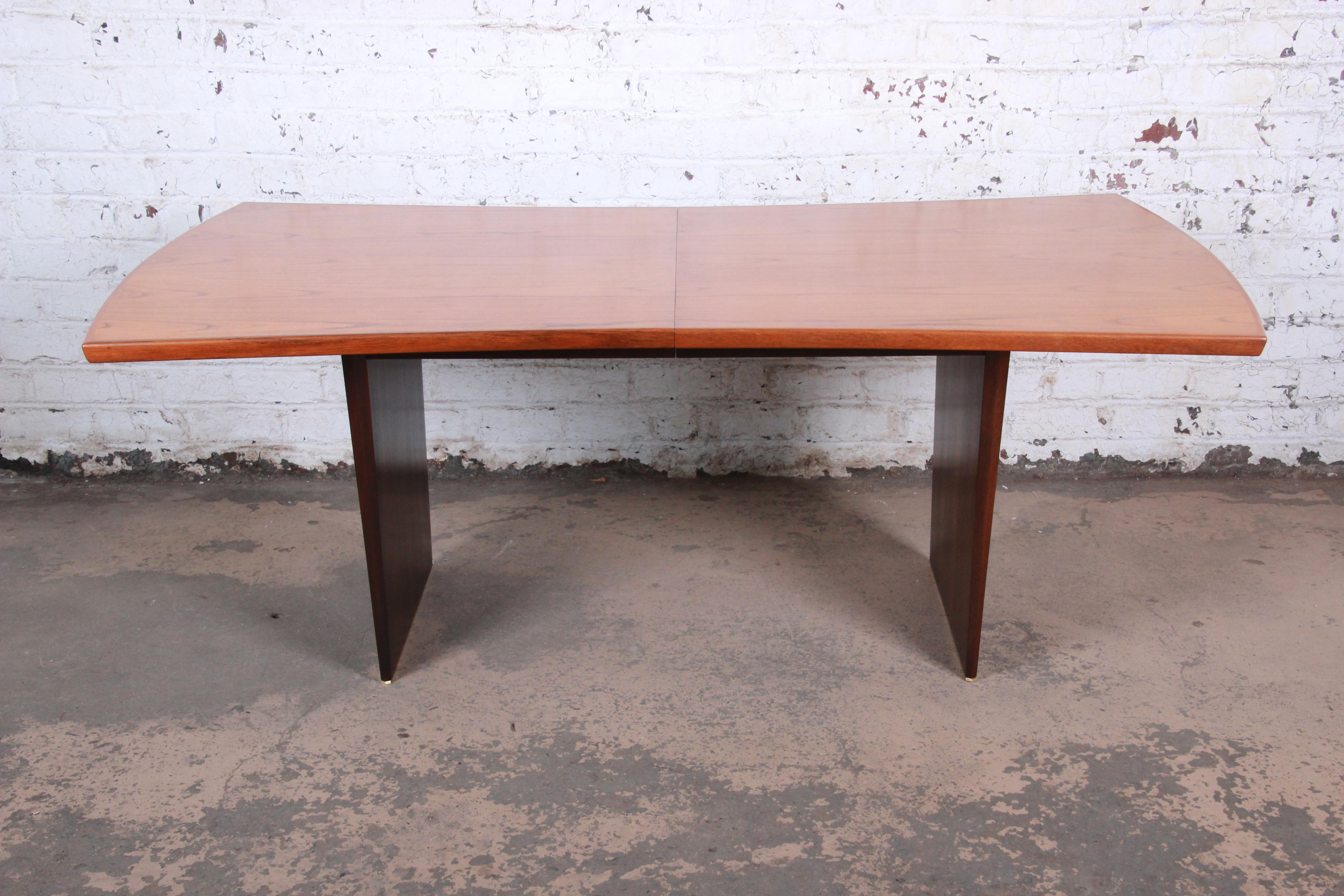 An exceptional Mid-Century Modern teak and walnut bow tie dining table designed by Harvey Probber. The table features a gorgeous teak wood top in a unique bow tie shape. It has tapered solid walnut slab legs with brass trim. Simple yet elegant in
