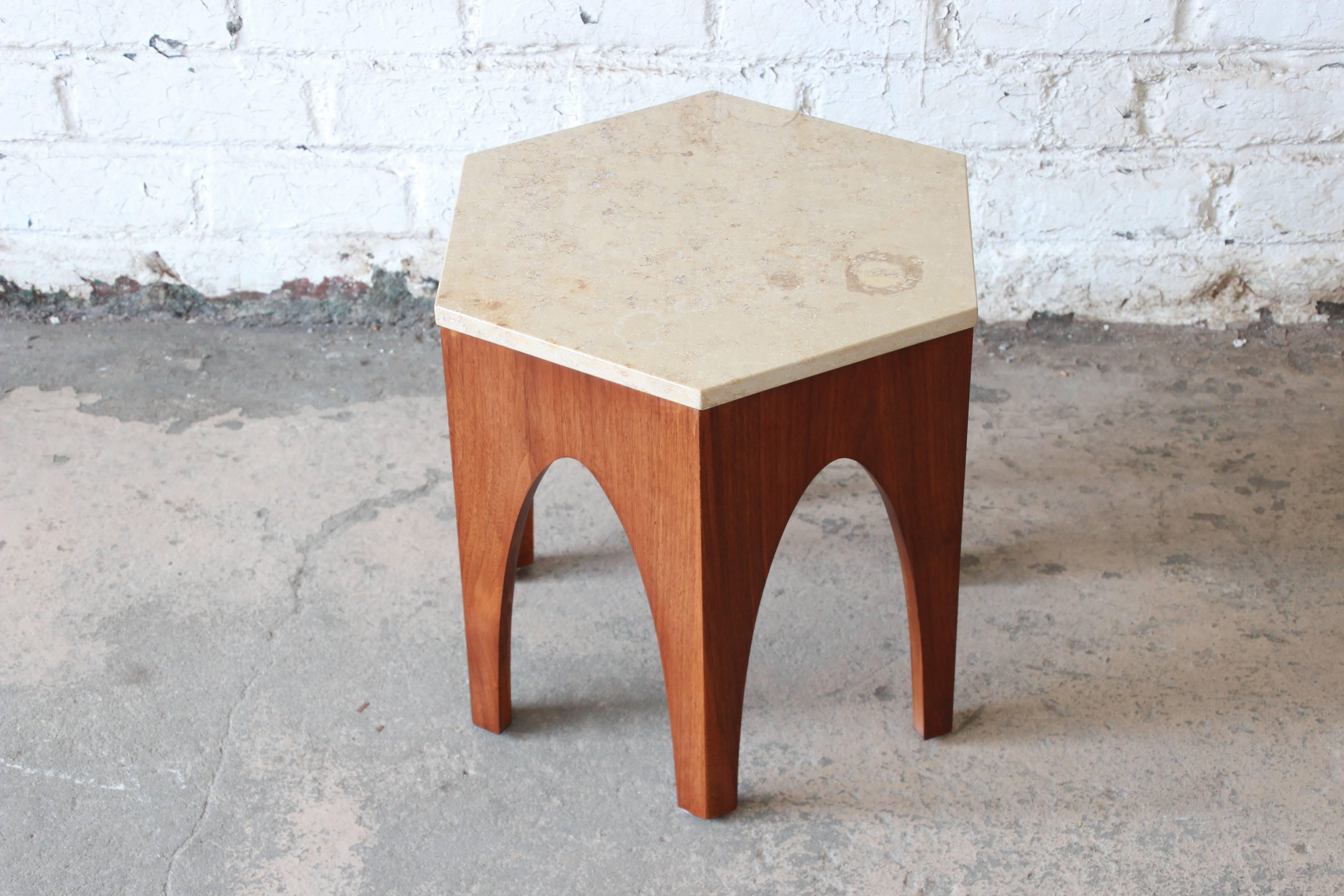 A beautiful Mid-Century Modern hexagon end or occasional table attributed to Harvey Probber. The table features an Italian travertine inset top over a sculpted walnut base with Moroccan inspired arches. It is finished on all sides and could also be