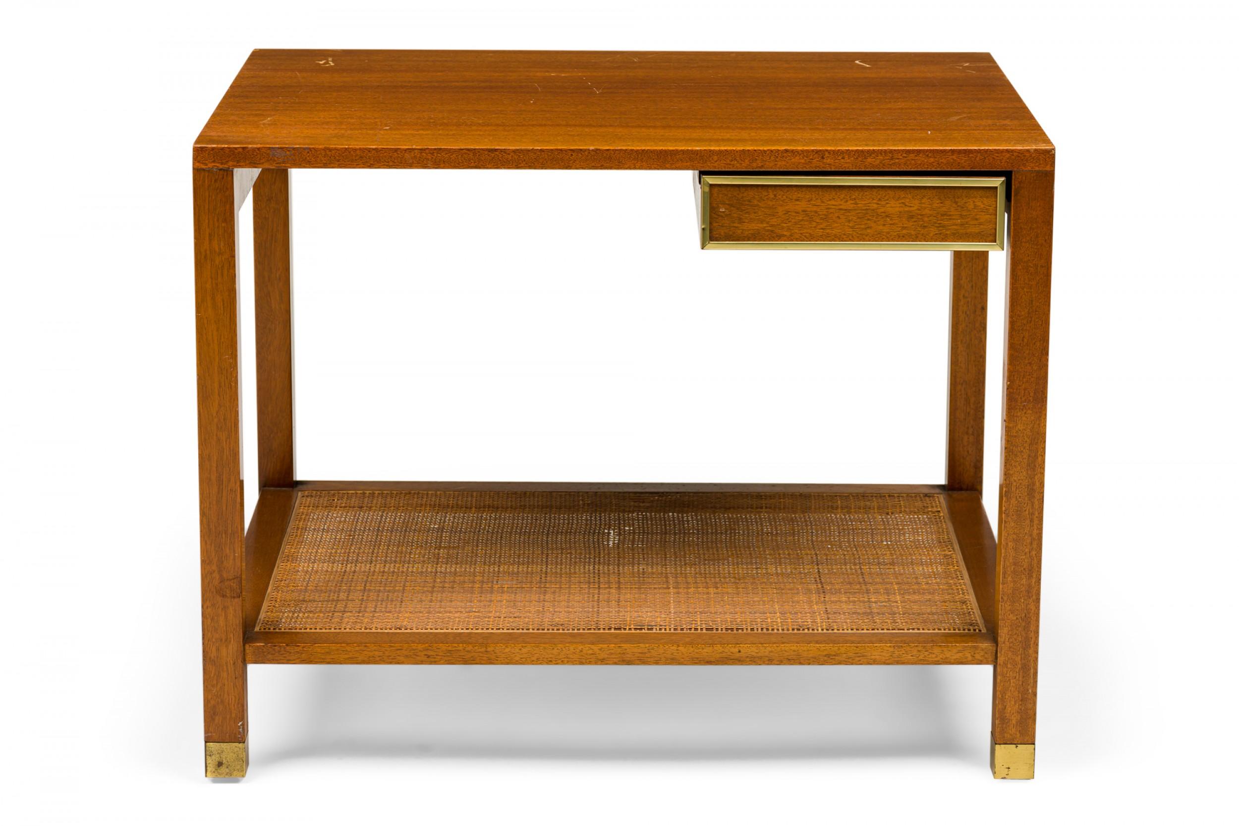 American Mid-Century Parsons-style end / side table with a rectangular wooden top over a single small side-oriented drawer with brass trim supported by four square wooden legs connected with a caned stretcher shelf and ending in brass sabots.