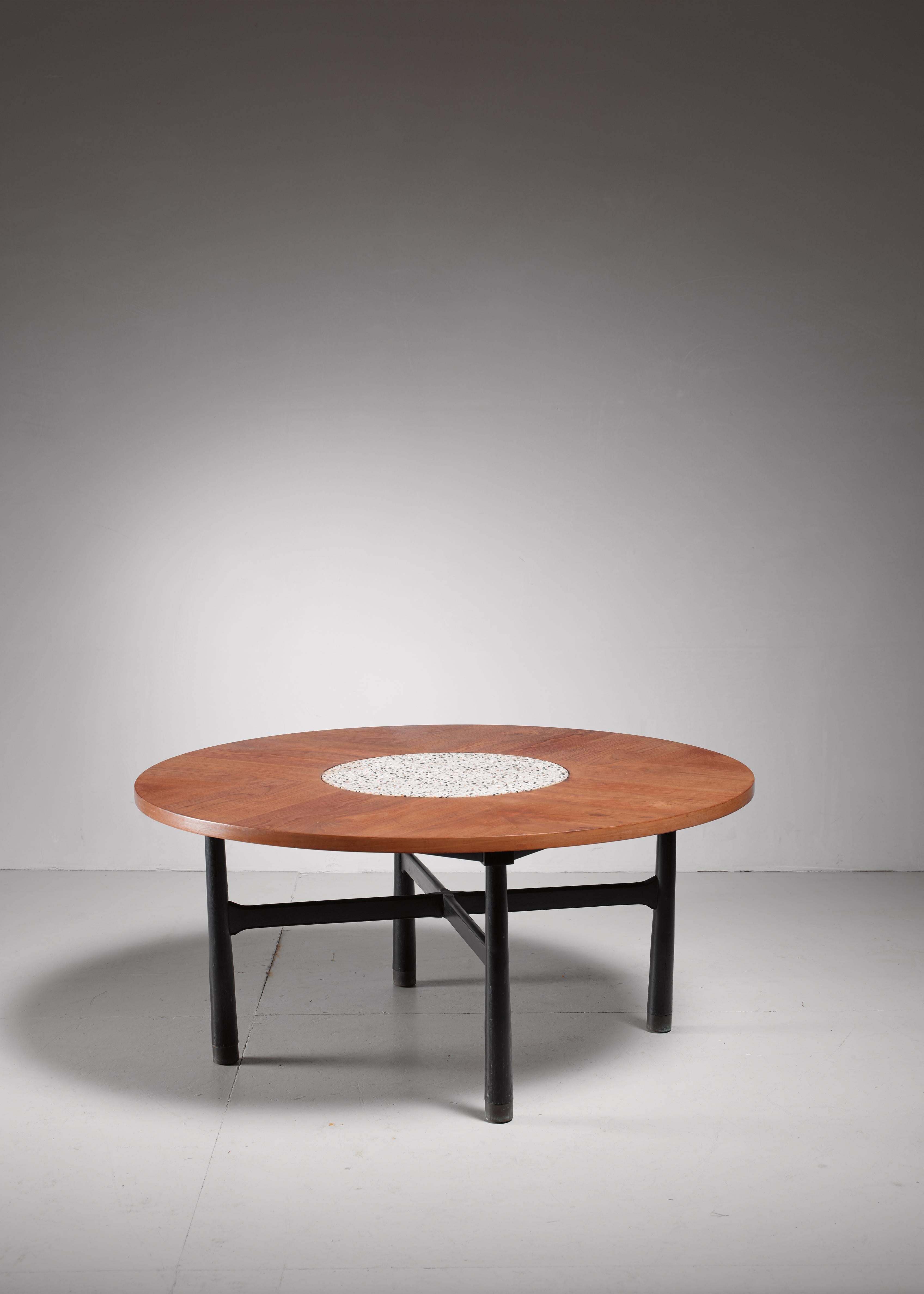 A round Harvey Probber coffee table. The walnut top rests on an ebonized wooden base with copper socks and a terrazzo stone circle in the centre.