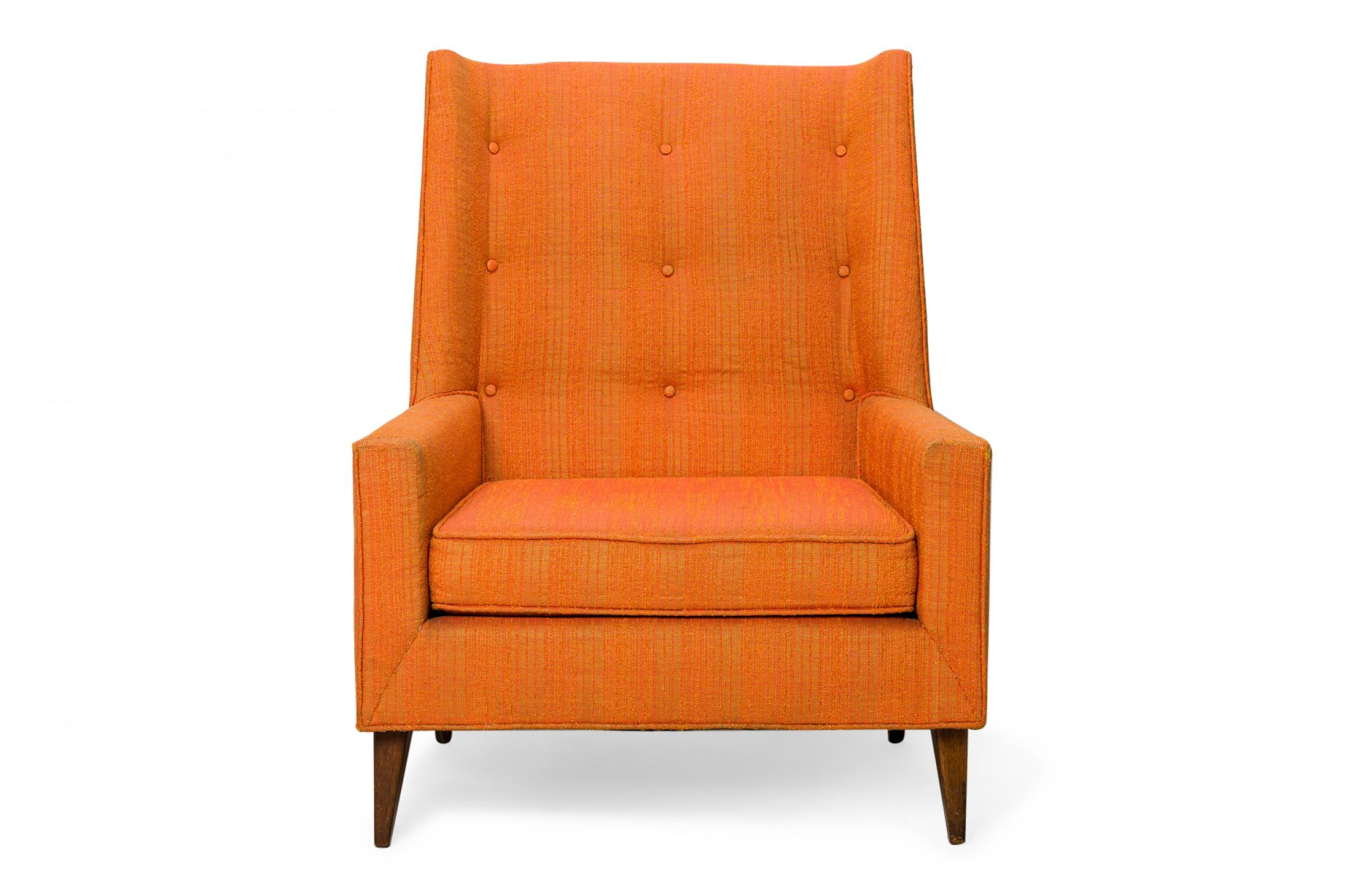 American mid-century arm / lounge chair with a tall back and button tufted textured orange upholstery, resting on four tapered wooden legs. (HARVEY PROBBER)
 