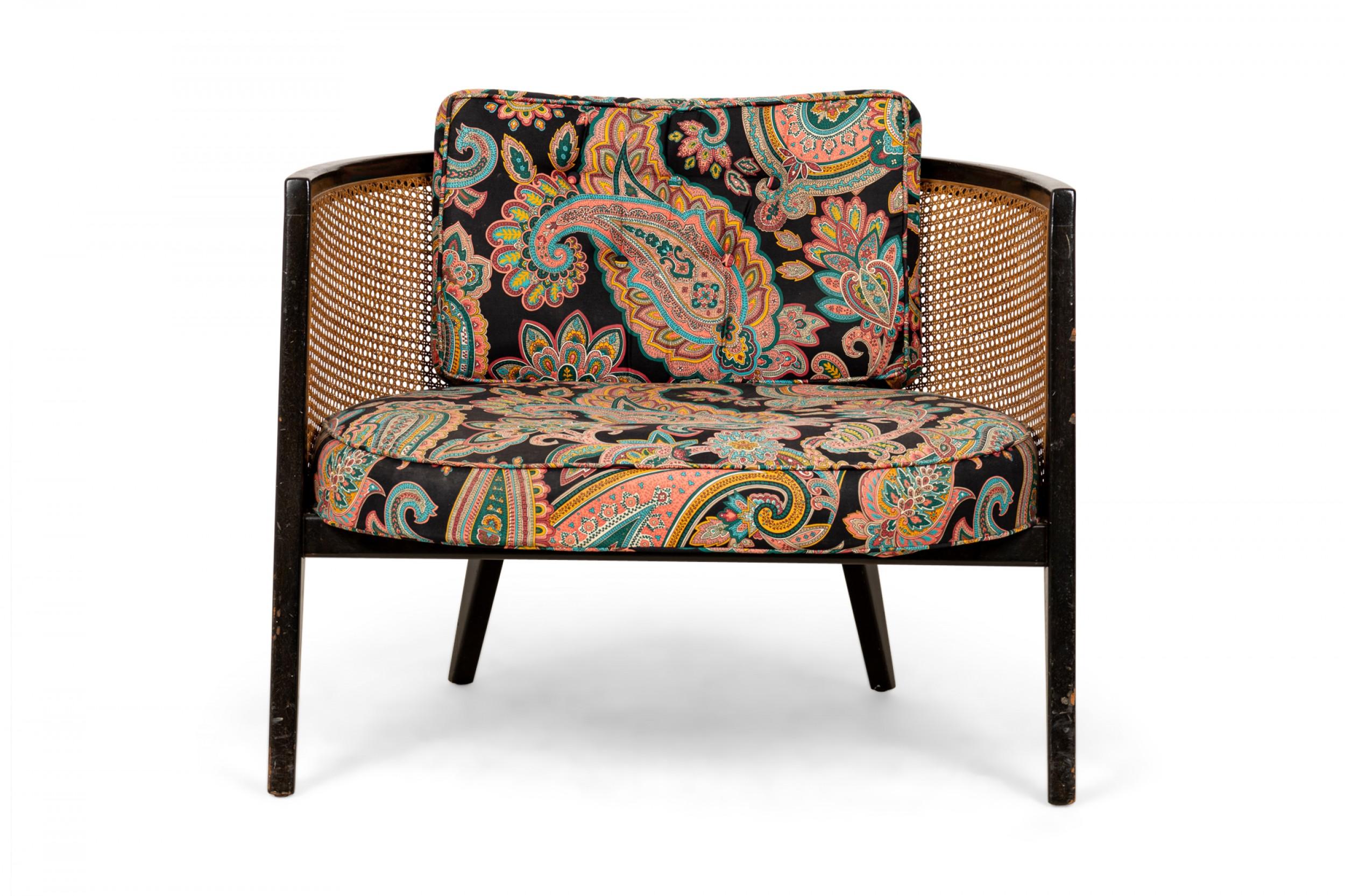 American mid-century hoop form lounge armchair with a curved ebonized wooden frame, caned back, seat, and sides, and a multicolored paisley patterned fabric upholstered seat and back cushion, resting on four angled tapered square legs. (HARVEY