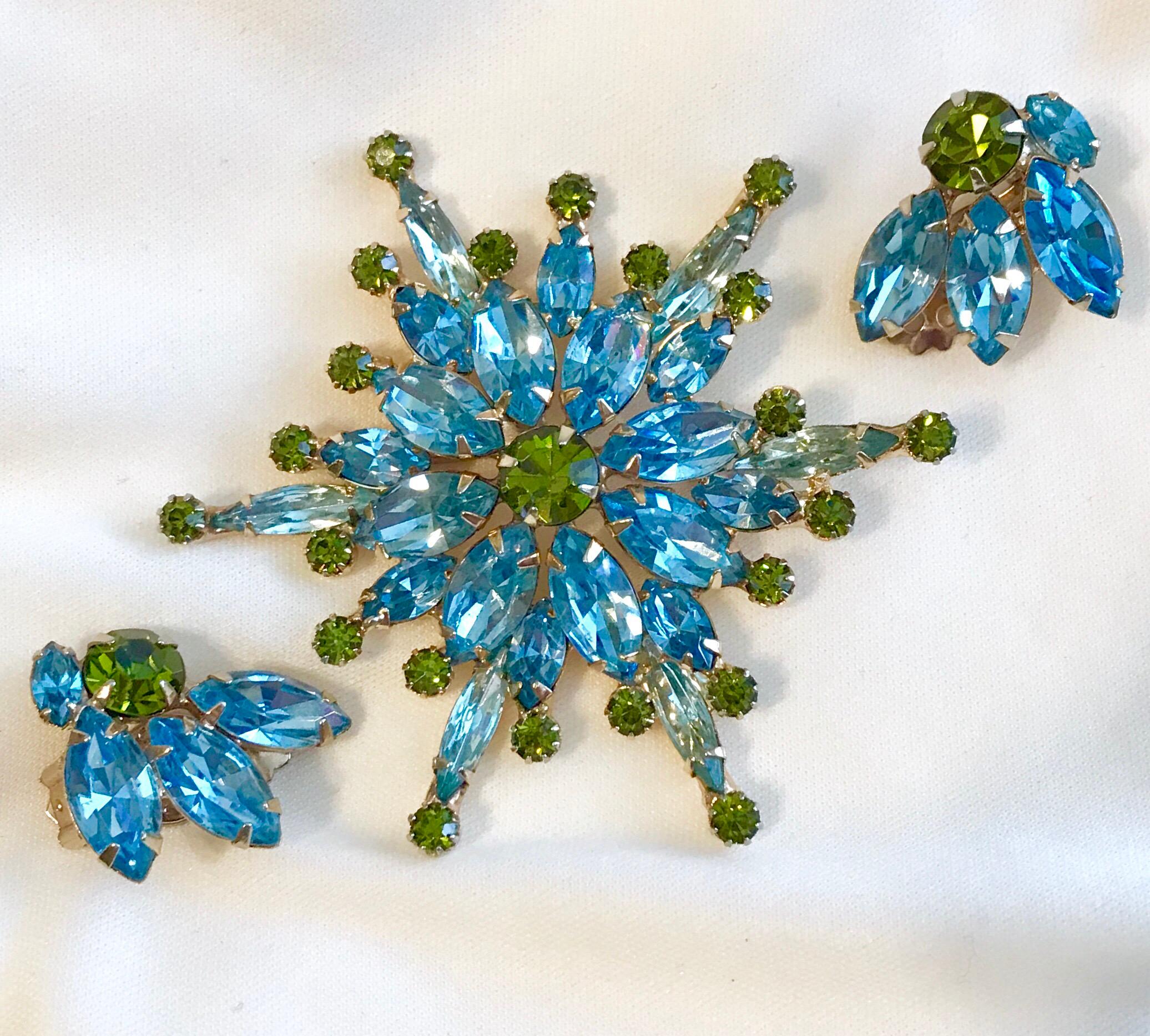 Circa 1960 Hattie Carnegie brooch and earring set.  The brooch, in a starburst design, is prong set with light blue faceted glass marquise and round faceted olivine green stones.  It measures 2.75