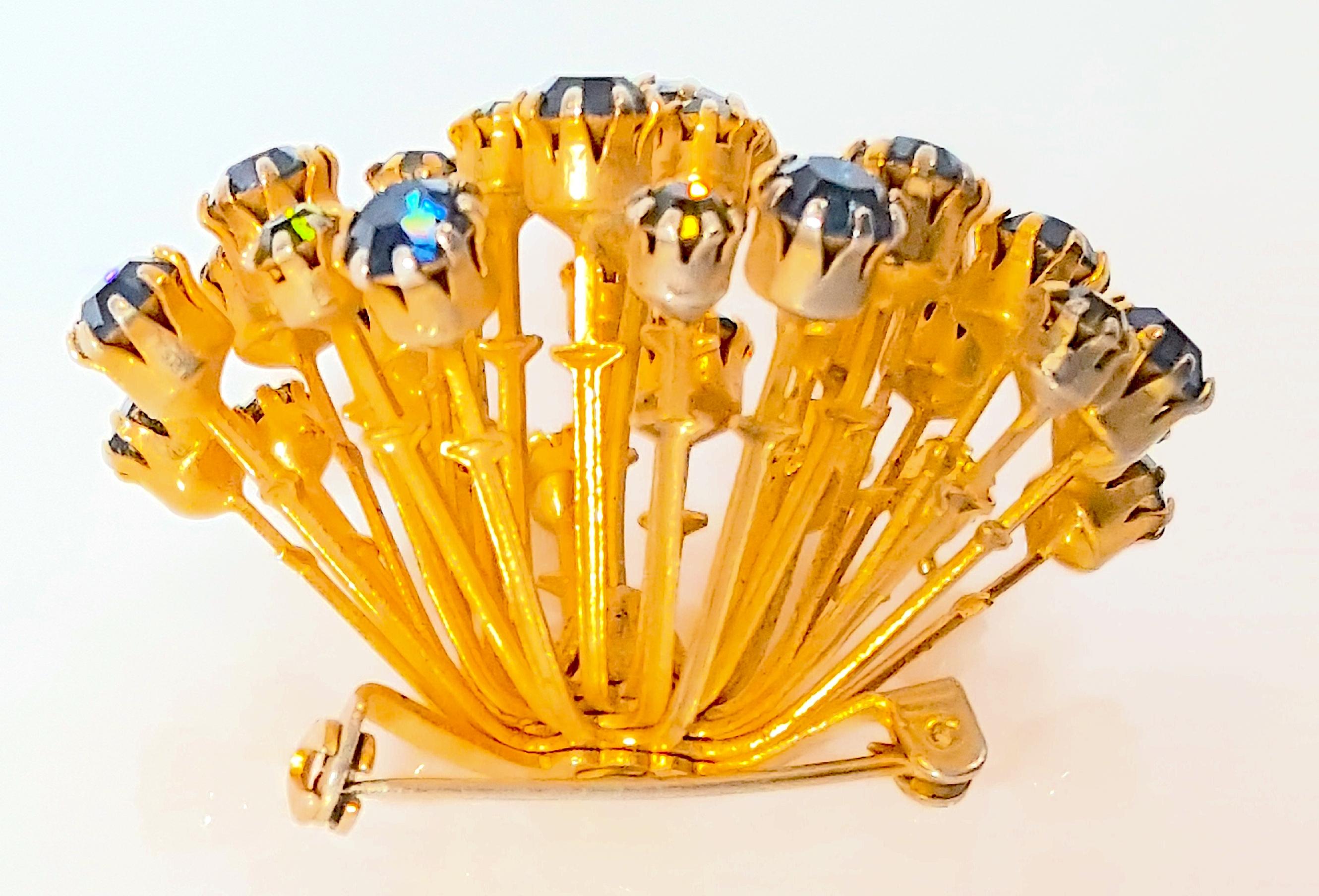 Hattie Carnegie commissioned for one of her mid-century clothing collections this modern starburst fireworks prong-set crystal convex brooch, whose gold-gilt metal rods cupping faux blue-sapphire and green-peridot round-cut glass are each bracketed