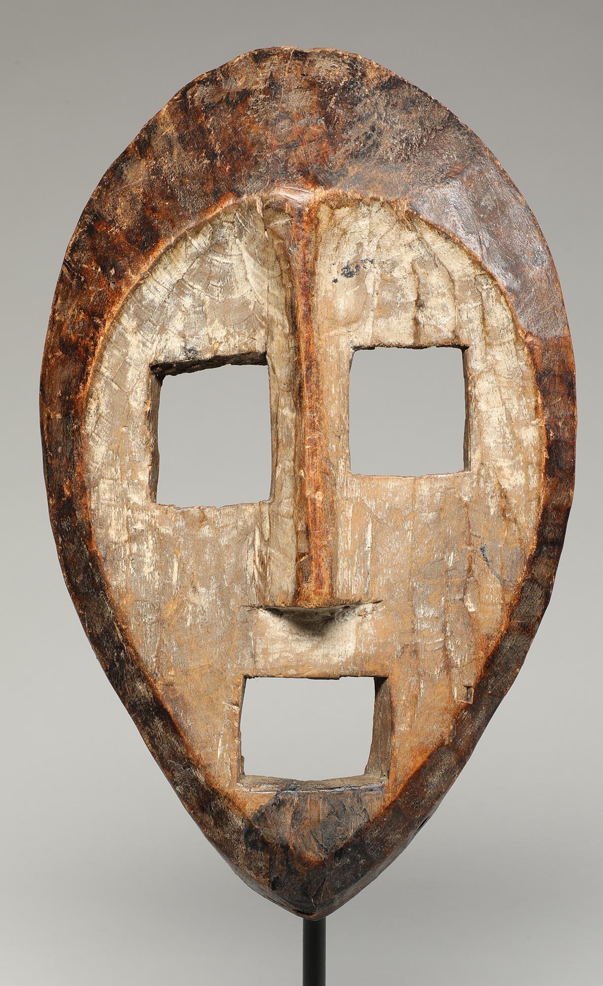 A haunting, carved wood Kumu mask with framed face, classic open square eyes and mouth typical of masks from this area. Face with remains of white framed by darker wood. Areas of wear, polish and age from tribal use. Early 20th century from the Kumu