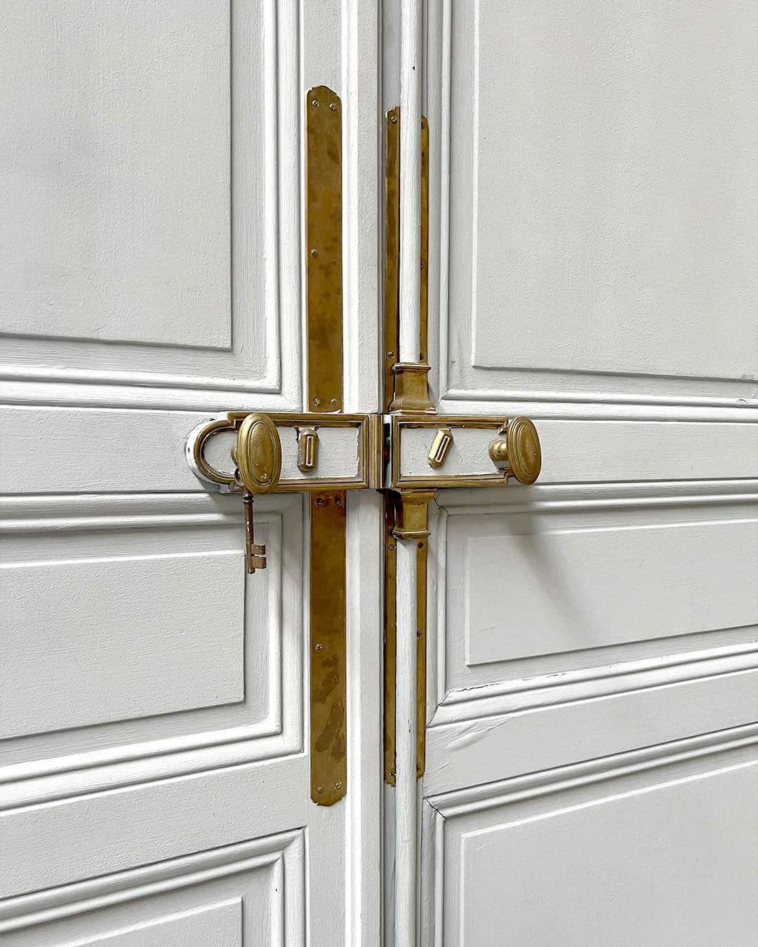Elegante porte à double battant de style haussmannien classique, dotée de lambris raffinés et de son système de quincaillerie et de serrure en laiton d'origine. Peint en blanc tendre, cet élément architectural apporte un charme parisien intemporel