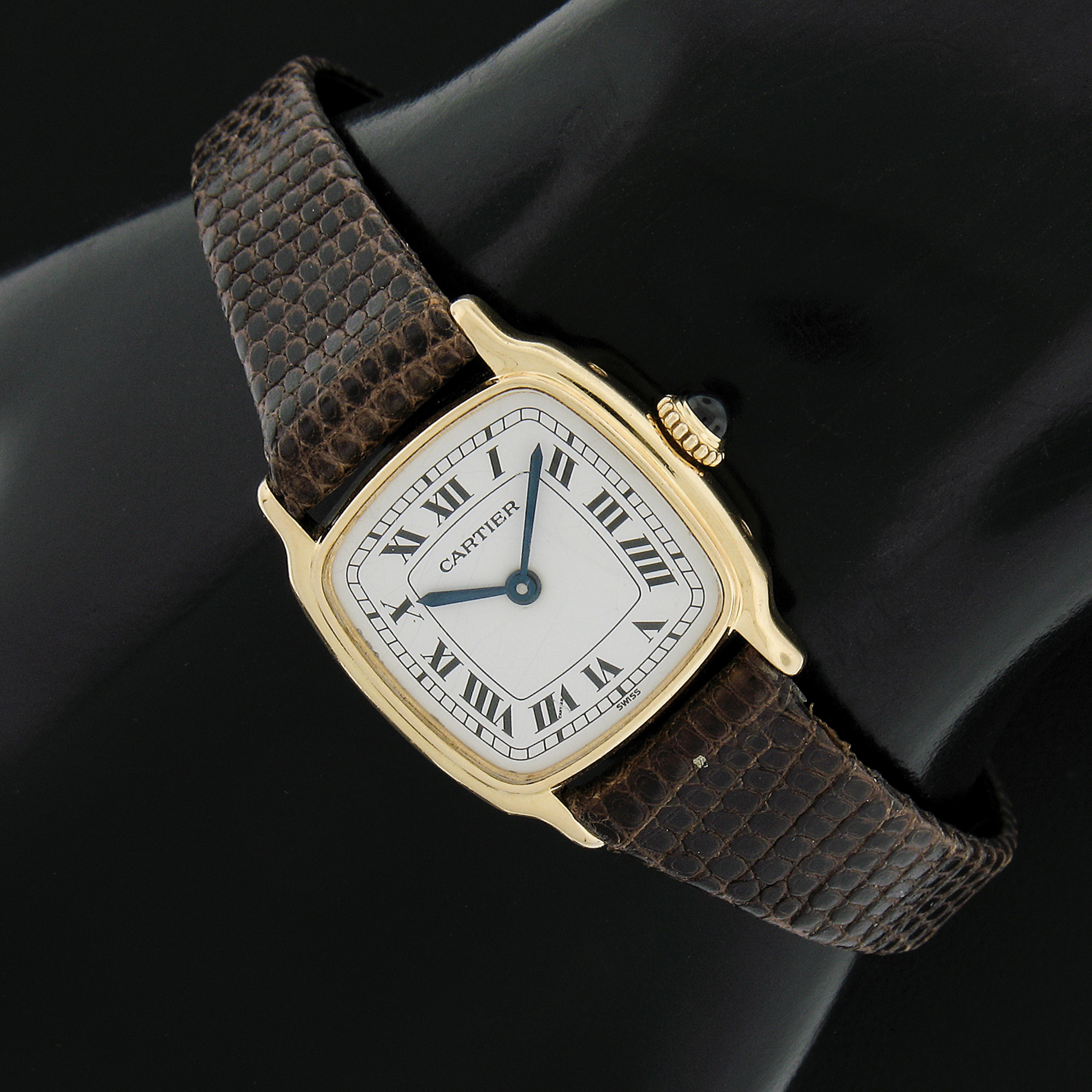 This beautiful classic vintage Cartier wrist watch features a mechanical hand wound Swiss movement mounted in an elegant, solid 18k yellow gold cushion shaped case. The watch comes with an aftermarket genuine lizard skin strap and a gold toned