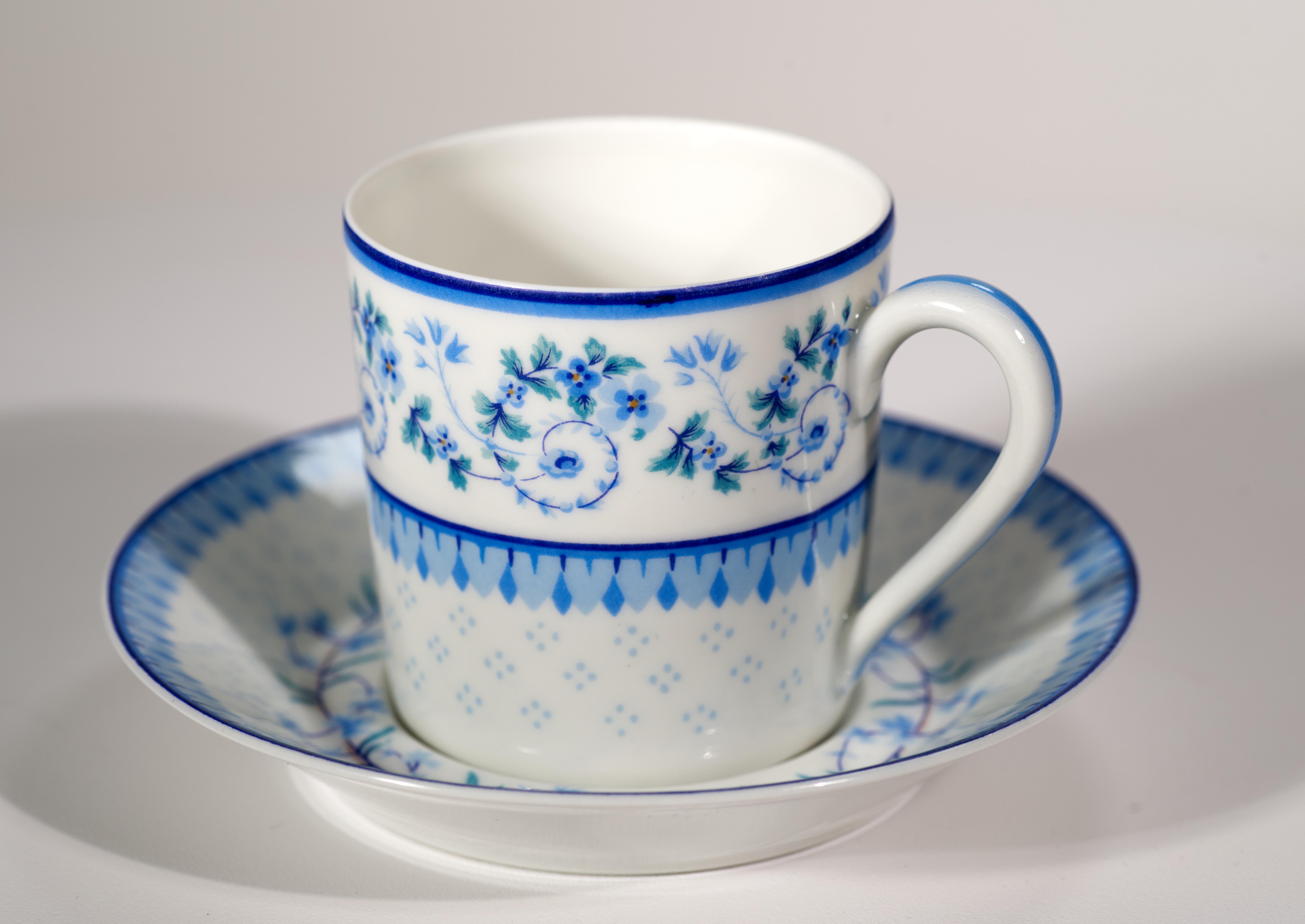  Rare vintage demitasse cup and saucer set is decorated in Corolle pattern with abstract geometric designs and flower garlands in shades of blue on white background. Cup and saucer rims are accented with thin cobalt blue bands, and the cup handle is