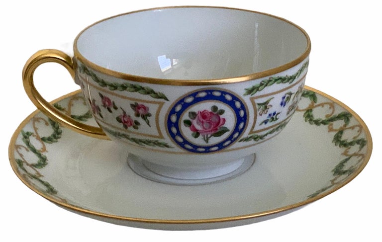 This is a Haviland Limoges hand painted porcelain wide mouth cup and saucer. It depicts bay laurel leaves garland in the upper border with a gilt rim. It is also adorned with a rose in the center surrounded by a laurel wreath. At each side of the
