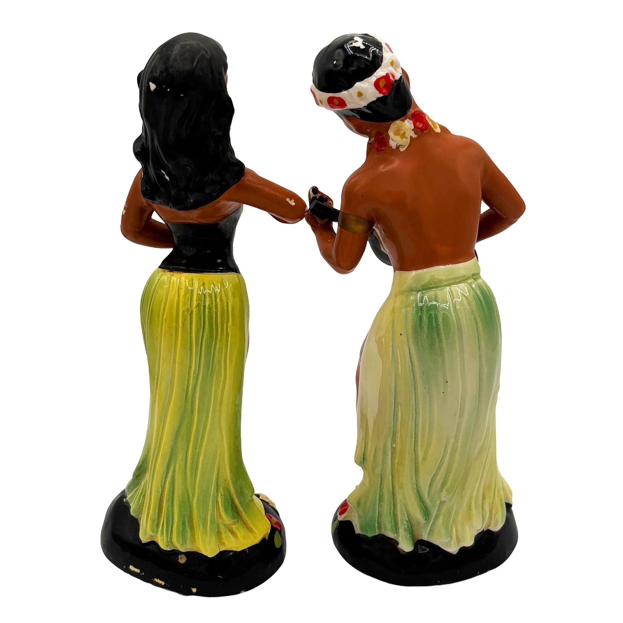 Pair of Mid-century Ceramic Hand-Painted Hula Girl & Ukulele Boy sculptures by Kreiss Company. Each captures the charm of Hawaiian culture from the post-war era with a matte paint finish and energetic expression. Both figurines are seated and