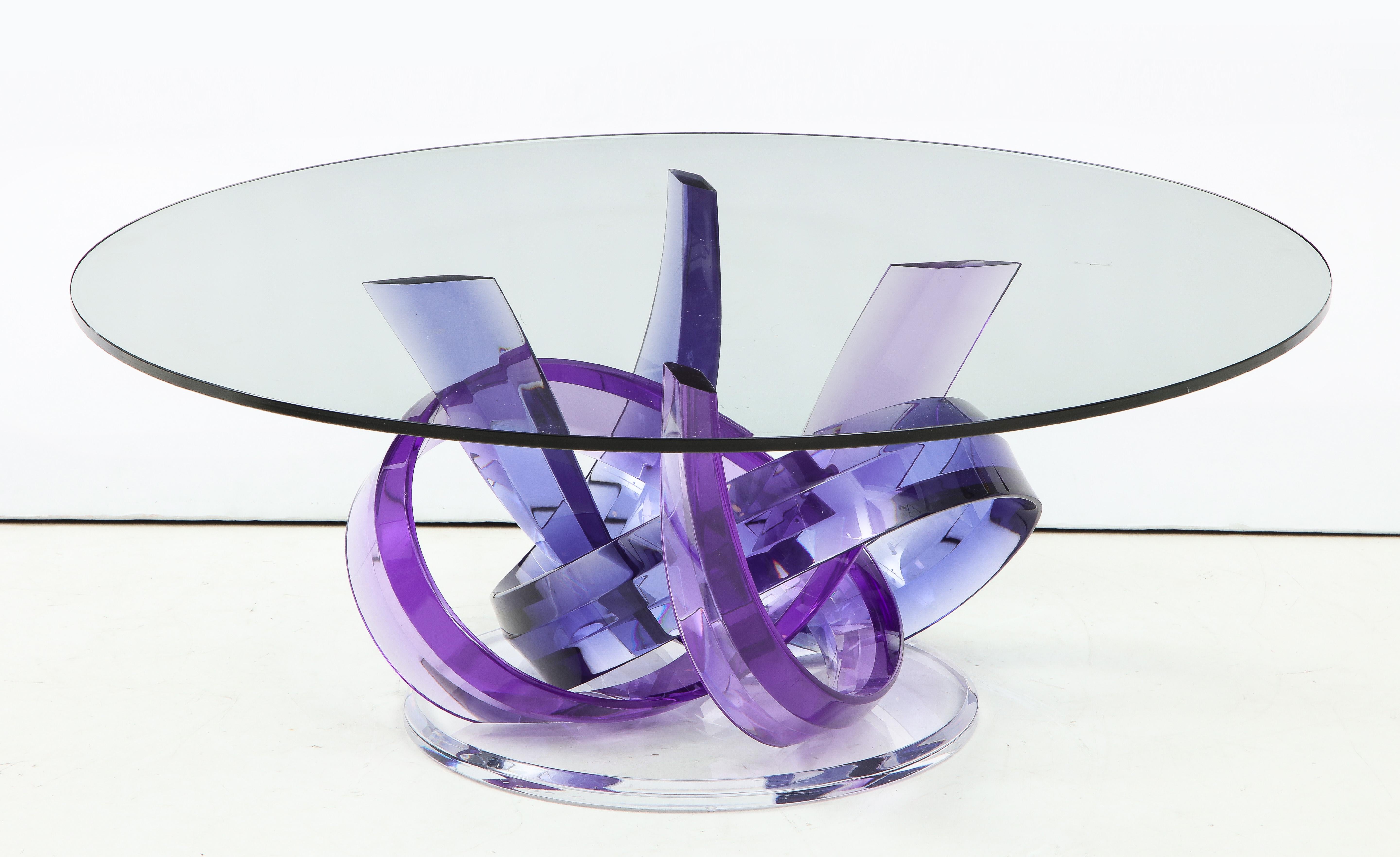 Exuberant Haziza coffee table featuring intertwined faceted acrylic bands in violet and indigo resting on a clear Lucite disc base. Labeled.