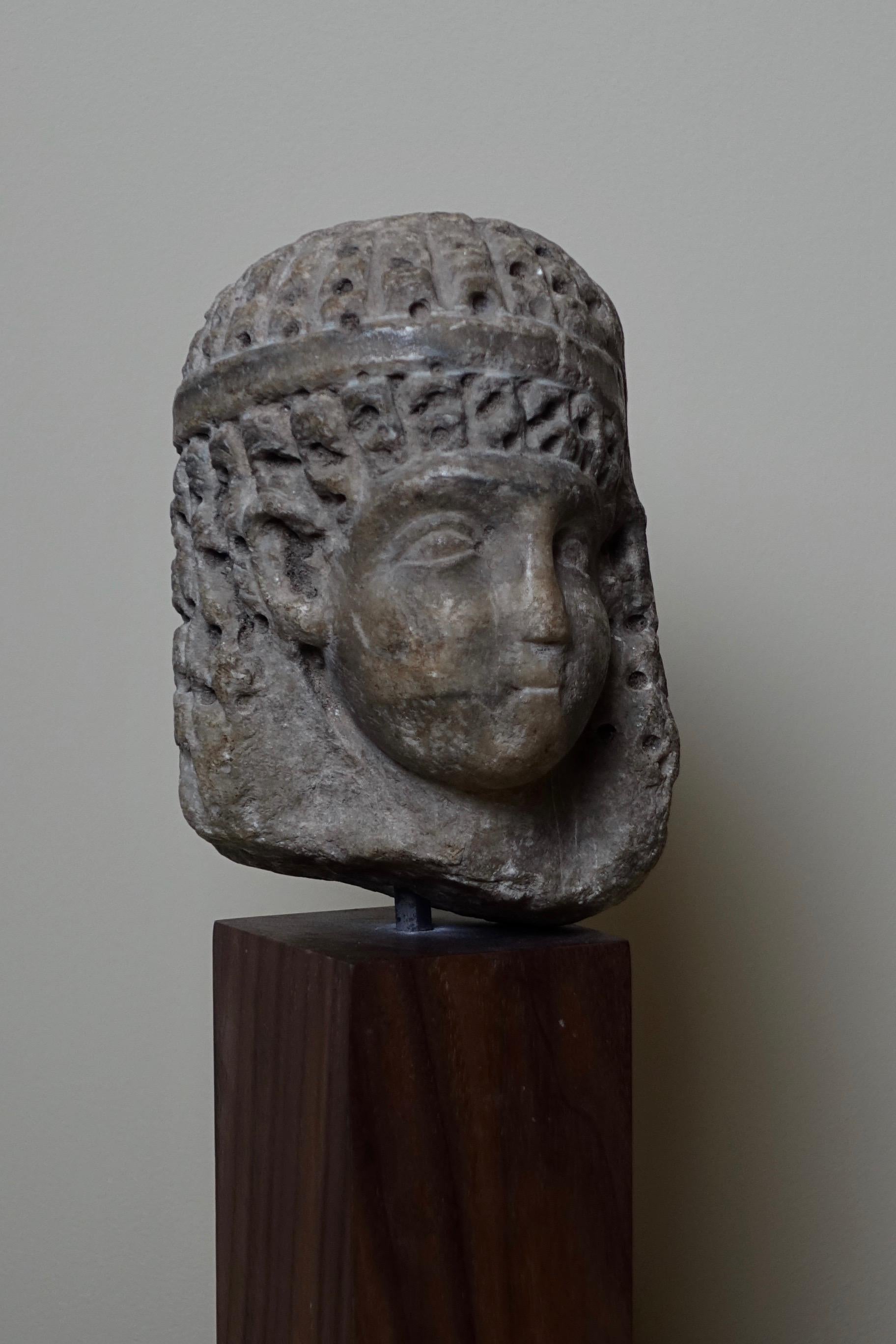 Gray marble head representing a woman with long curly hair and idealized features, wearing a tiara in the form of a simple band. The idealized face is inspired by the models developed since the Old Kingdom and presents conventional features: a very