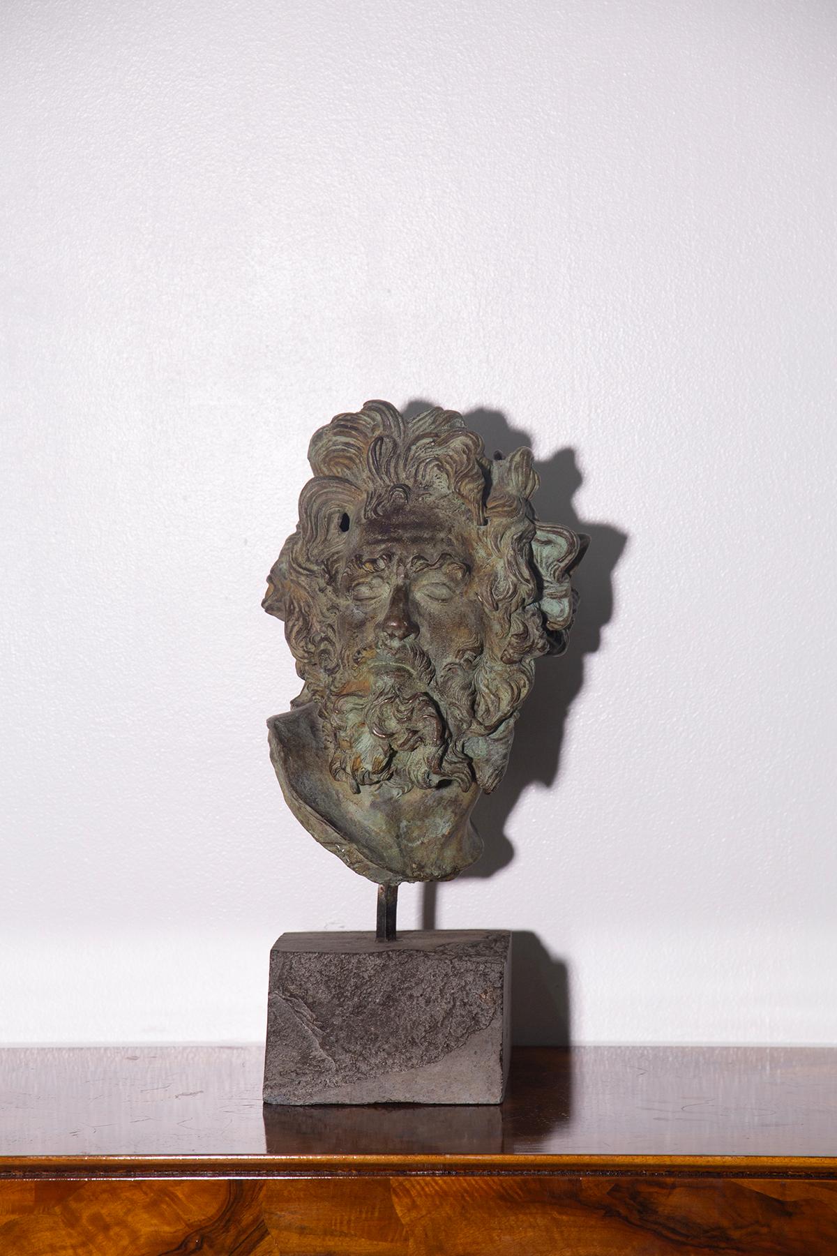 This fascinating bronze sculpture depicts a male head with an expressive and deeply classical face, characterized by thick hair and a beard sculpted with great detail. This is a patinated bronze Head of Lacoon, made in the 20th century, which