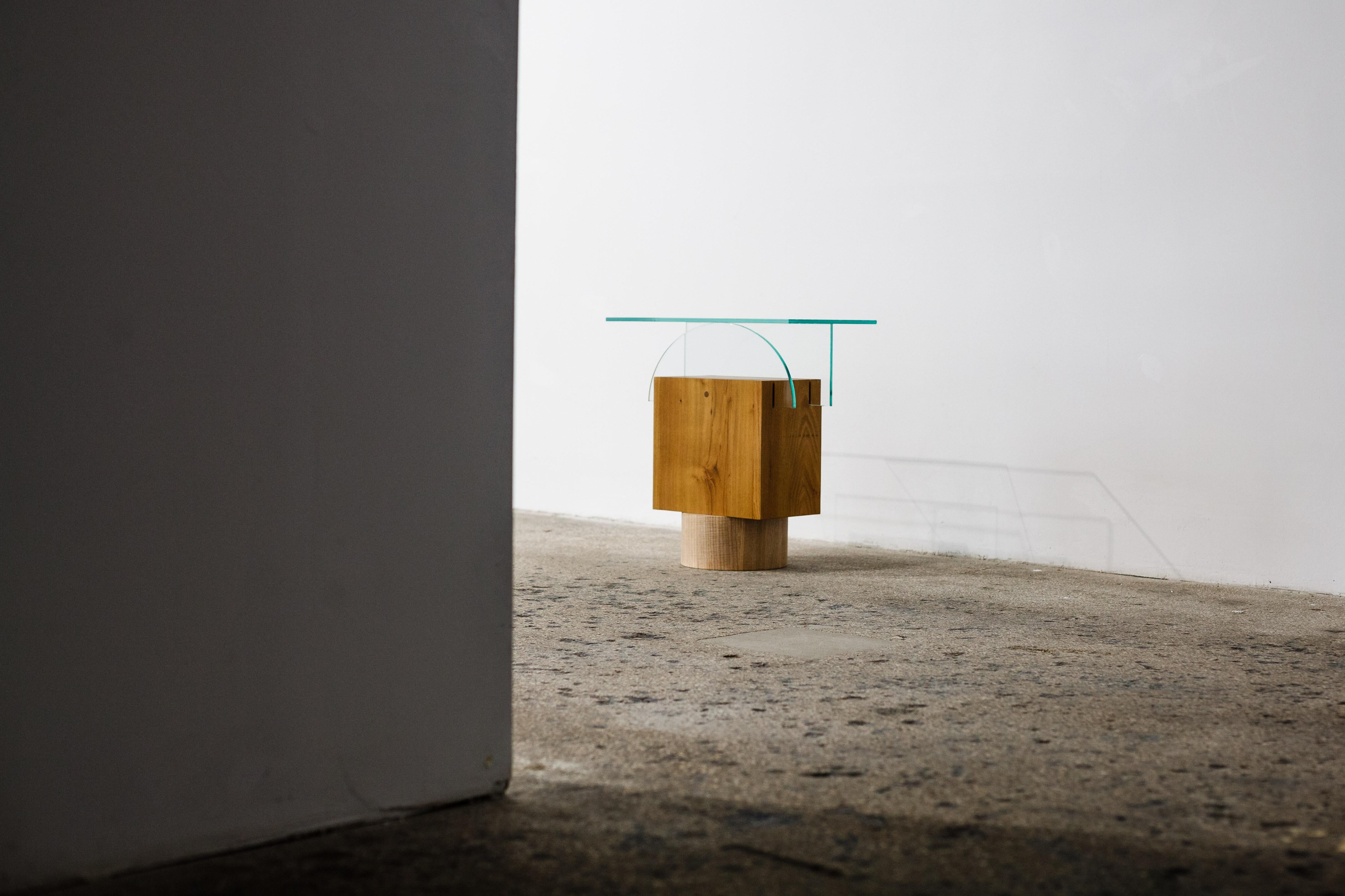 A composition of acacia and ash wood with glass, that serves as a side table/object. The piece is part of a series named Form before function, composed of side objects and open cabinets, with an aesthetic that places the objects closer to a