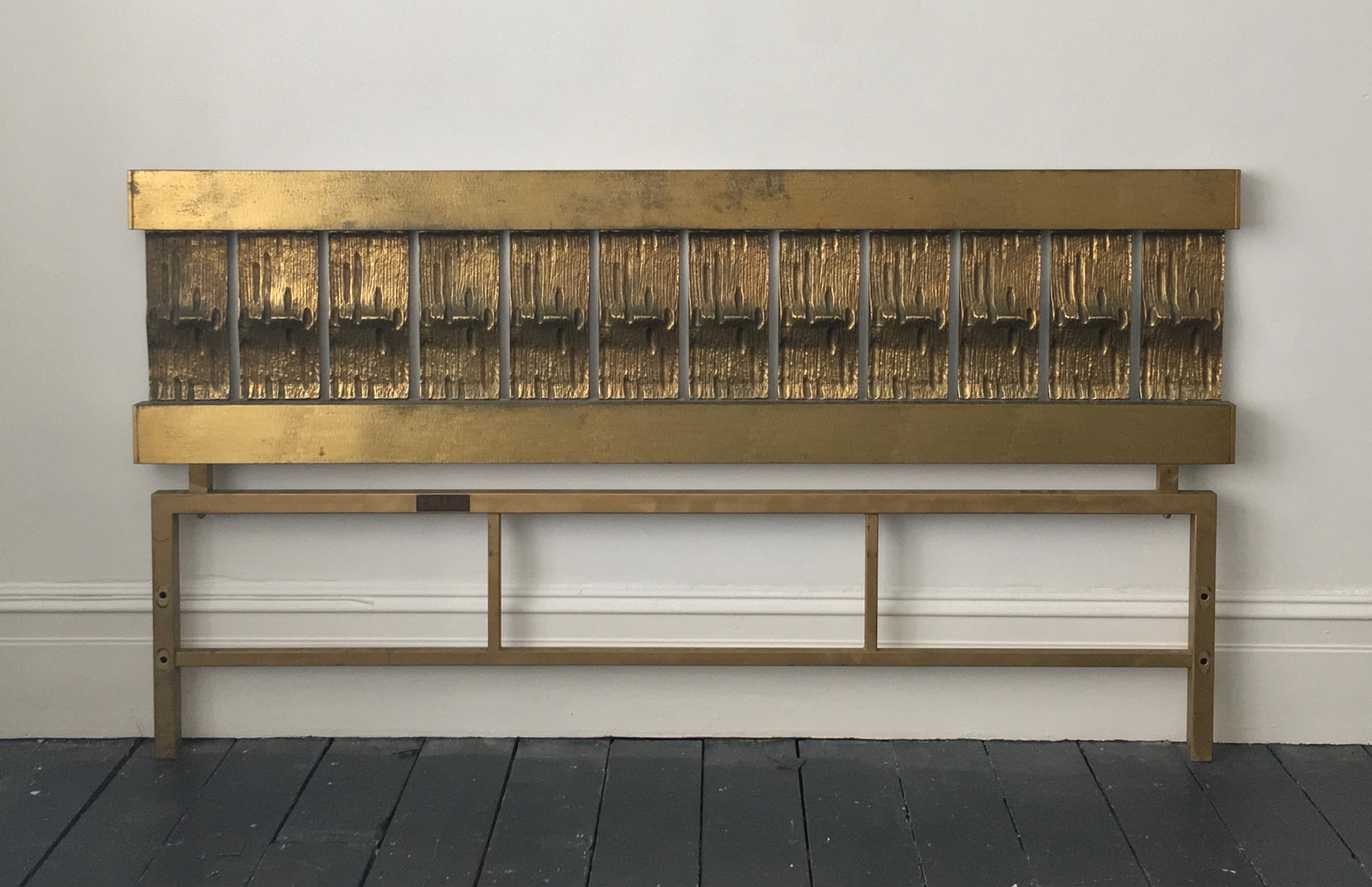 A headboard of cast and hammered brass, by Luciano Frigerio, Italy, mid-20th century.

This is a statement piece, with a simple block-like construction, which gives it a strong Brutalist feel. The upper section comprises two cross-bars with