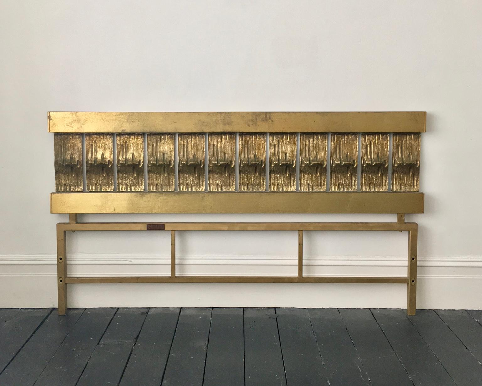 A mid-century modern headboard of cast and hammered brass, by Luciano Frigerio, Italy.

This is a statement piece, with a simple block-like construction, which gives it a strong Brutalist feel. The upper section comprises two cross-bars with