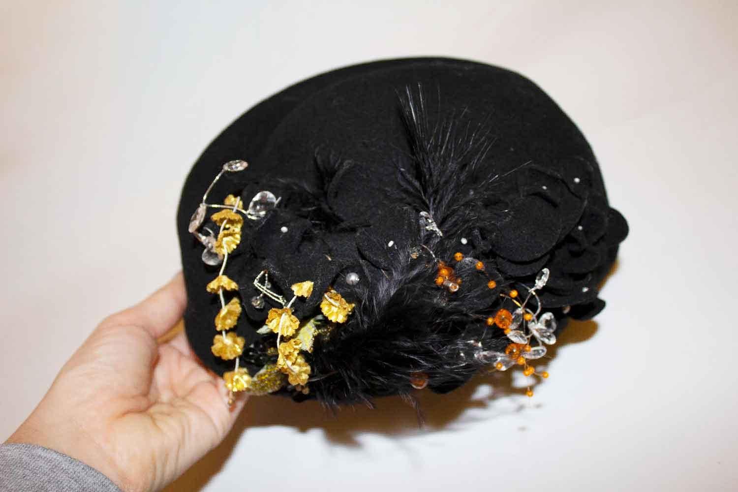 A stunning and headturning  black hat by Hamama, Russia. The hat has flower, bead and feather details, and measures, internal circumference 24'', height 6 1/2''.
