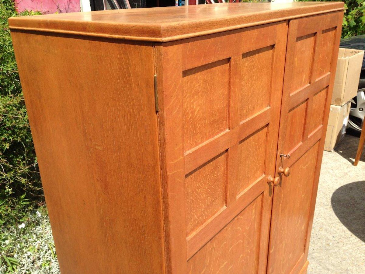 Heals. An Arts & Crafts oak tallboy, compactum wardrobe or nursery chest with hanging space to the left and a fitted drawer section to the right.

 