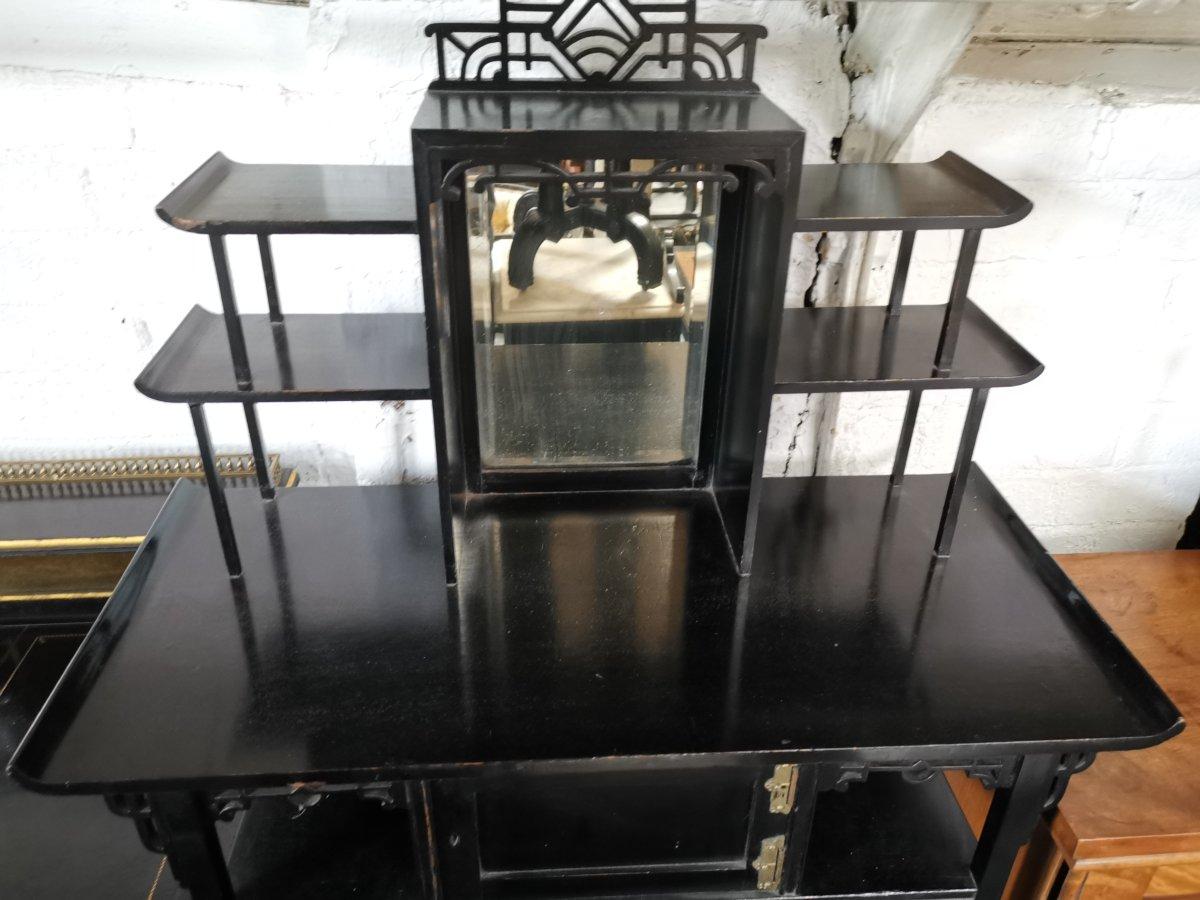 Heals Attributed. An Anglo-Japanese Ebonised small 'Pagoda' style side cabinet with a fretwork, mirrored and shelved top, the base with an asymmetric arrangement of a cupboard and shelves with splayed legs.

 