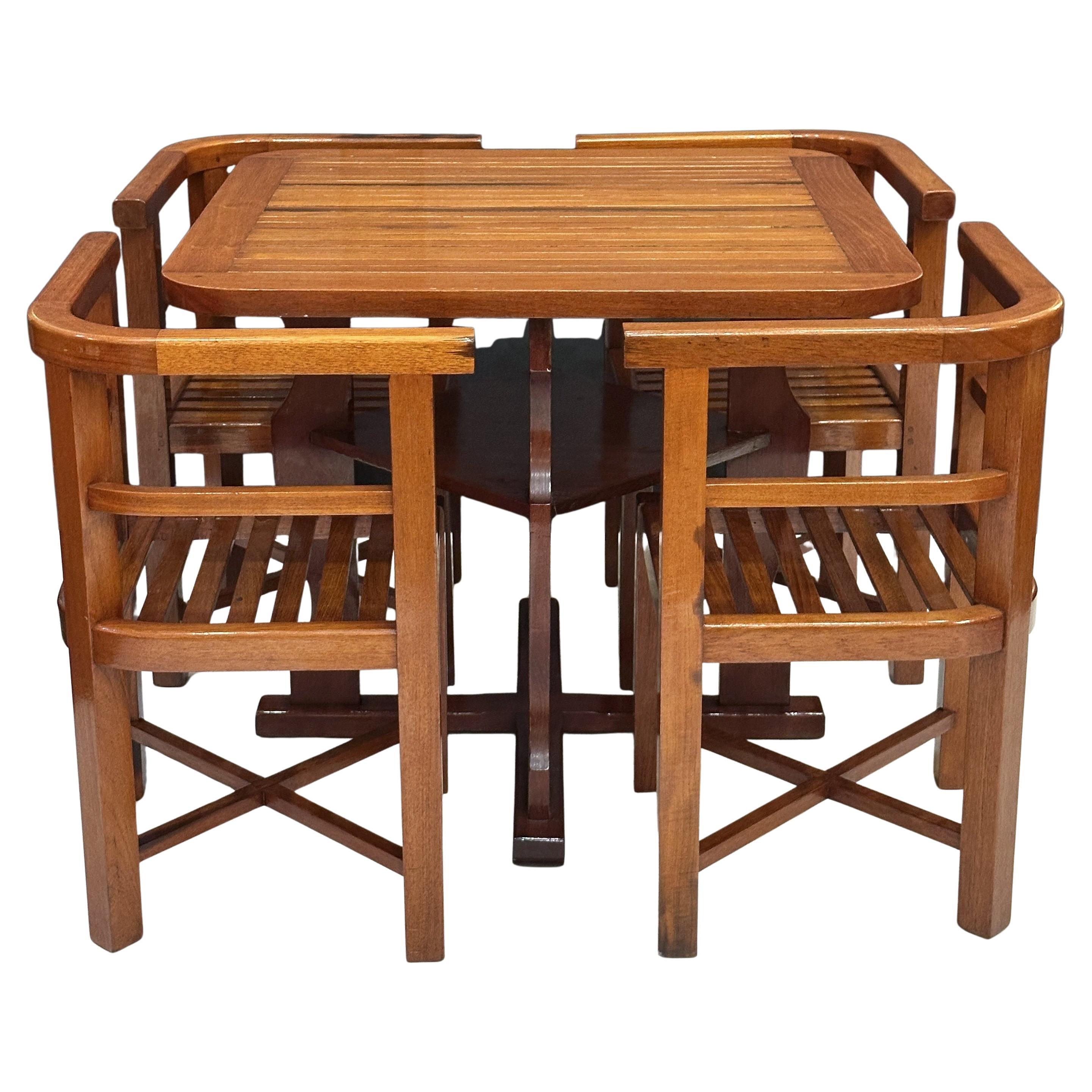 A handsome modular card table with four fitted chairs, circa 1930s - from the celebrated English design company, Heal’s. The mahogany table featuring a slatted top with rounded corners over a fitted base with under tray, set upon a cross-legged